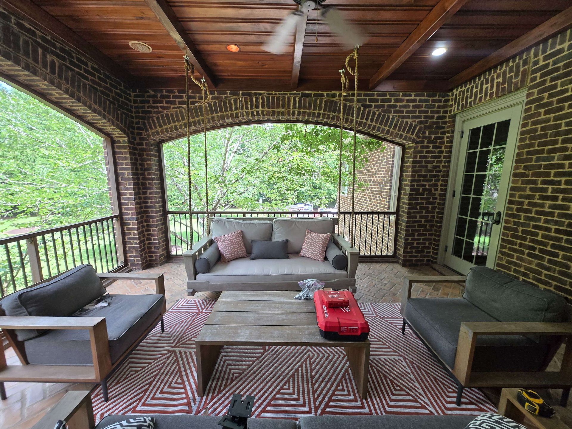 Covered porch with wicker seating, patterned rug, and wooded view through arched opening