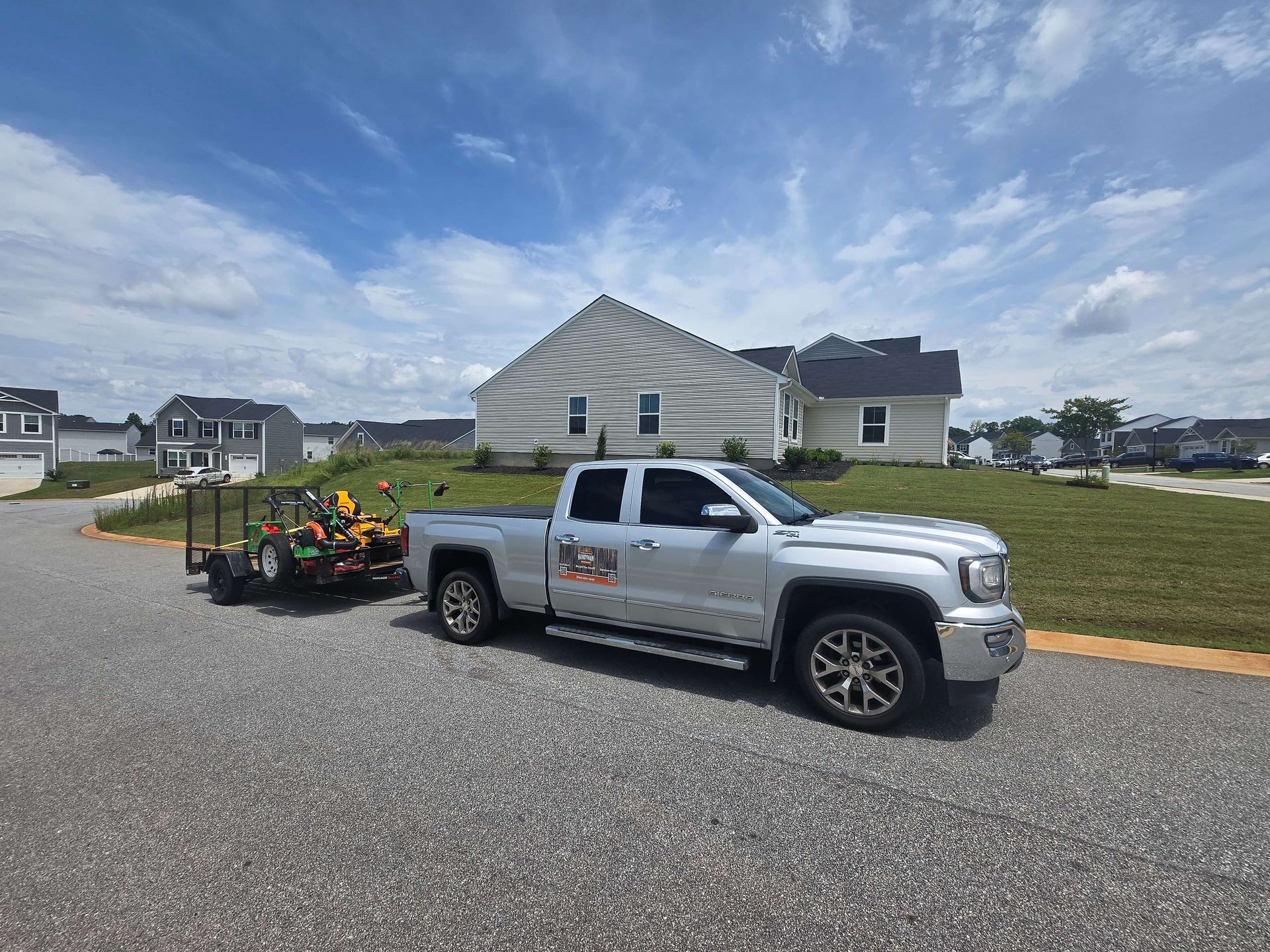 Silver pickup truck towing a trailer of flowers on a suburban street with houses and blue sky