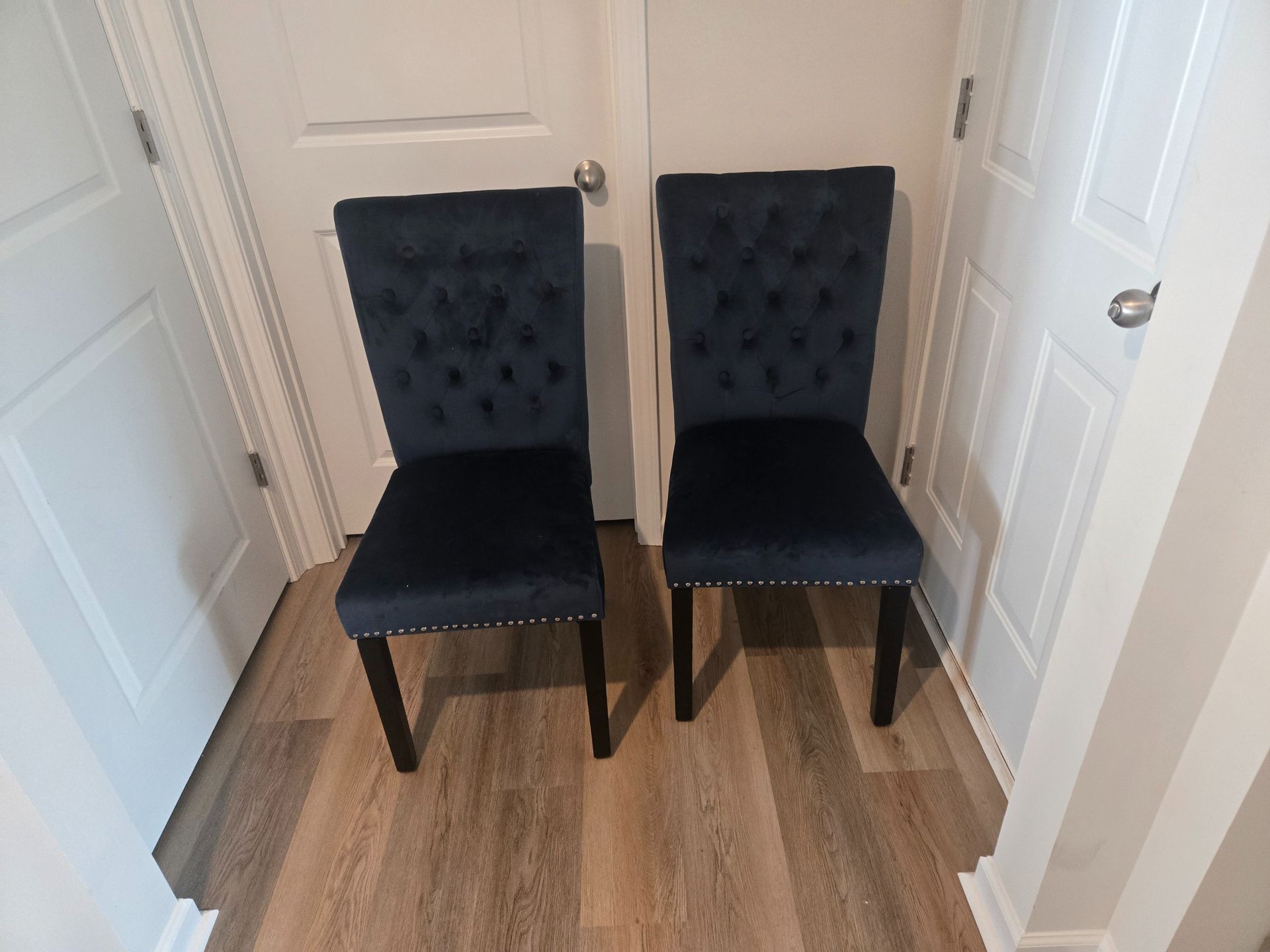 Two black tufted chairs in a small hallway with white doors and wood flooring