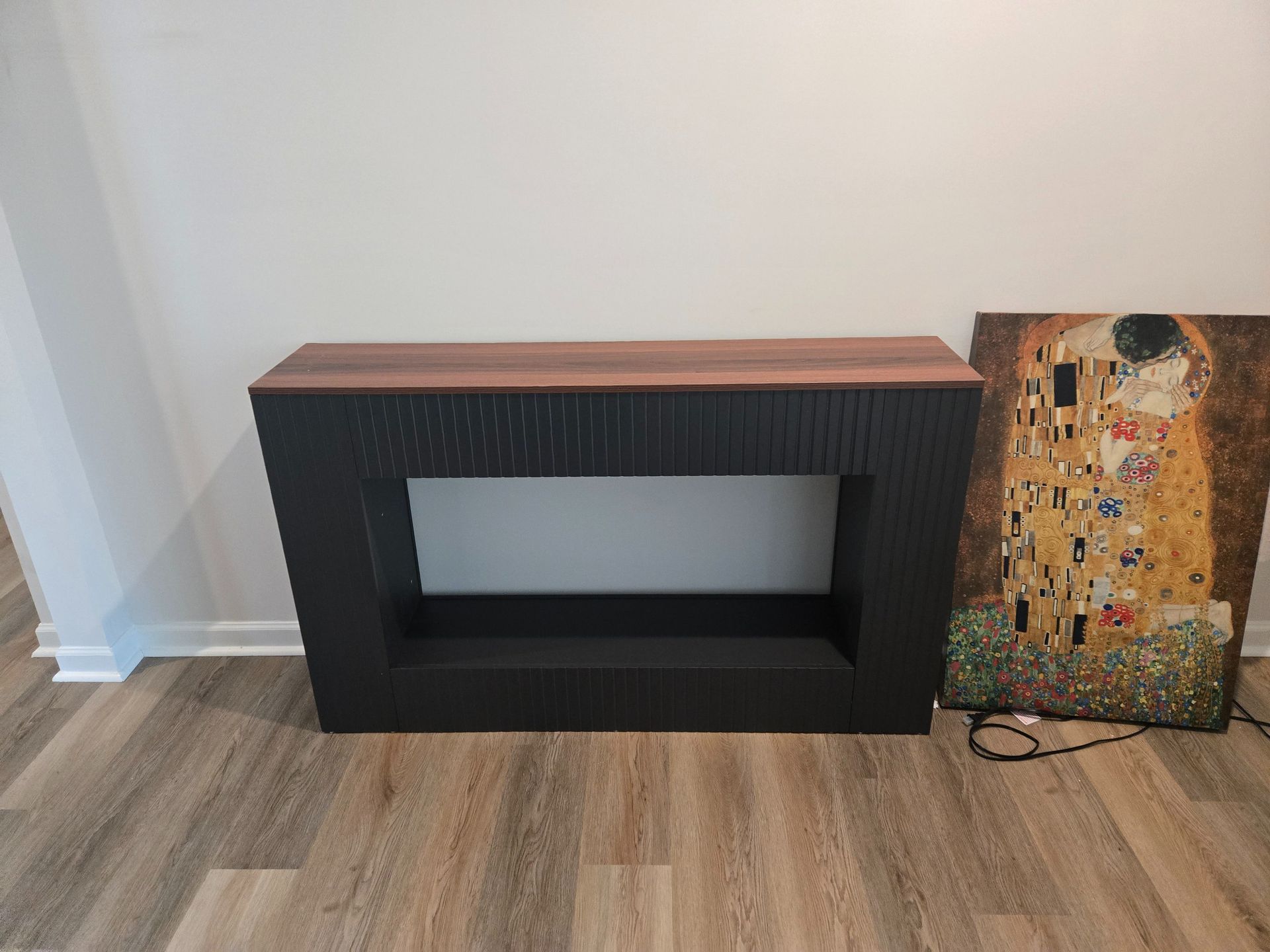 Black fireplace surround with wooden top beside colorful abstract artwork on a wood floor