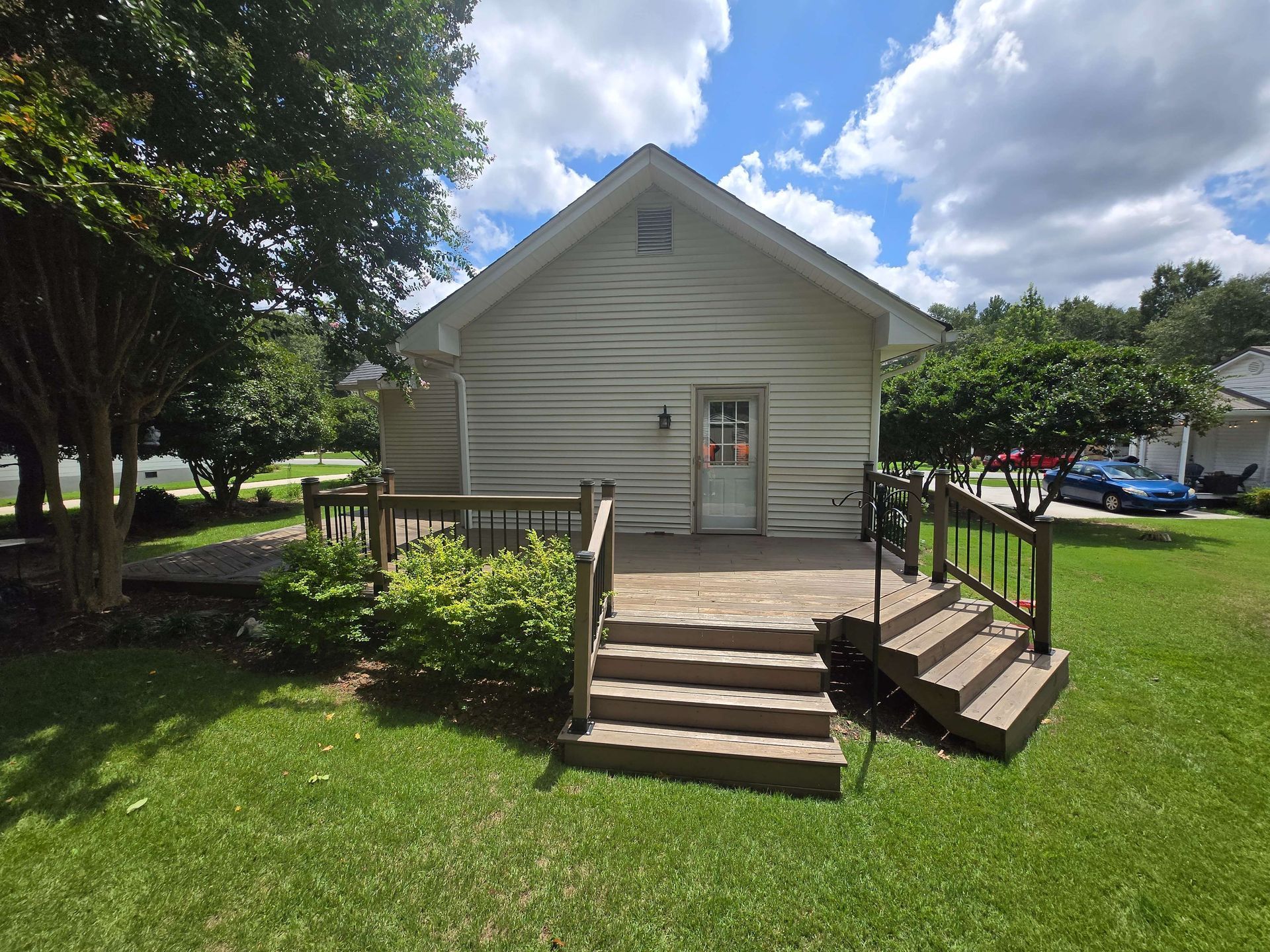 Small beige house with front steps and ramp, set on a grassy lawn under a partly cloudy sky.