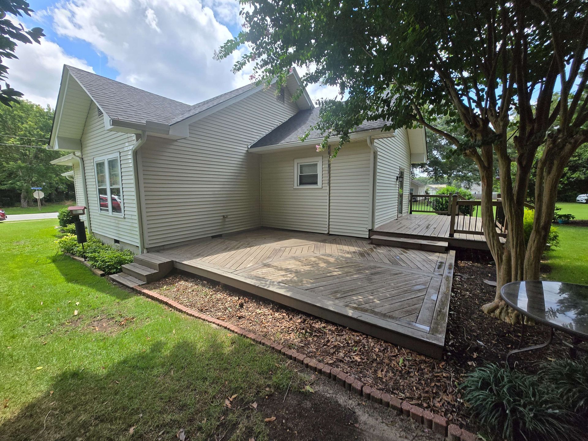 White house with a warped roof and damaged porch beside a tree and yard after storm damage