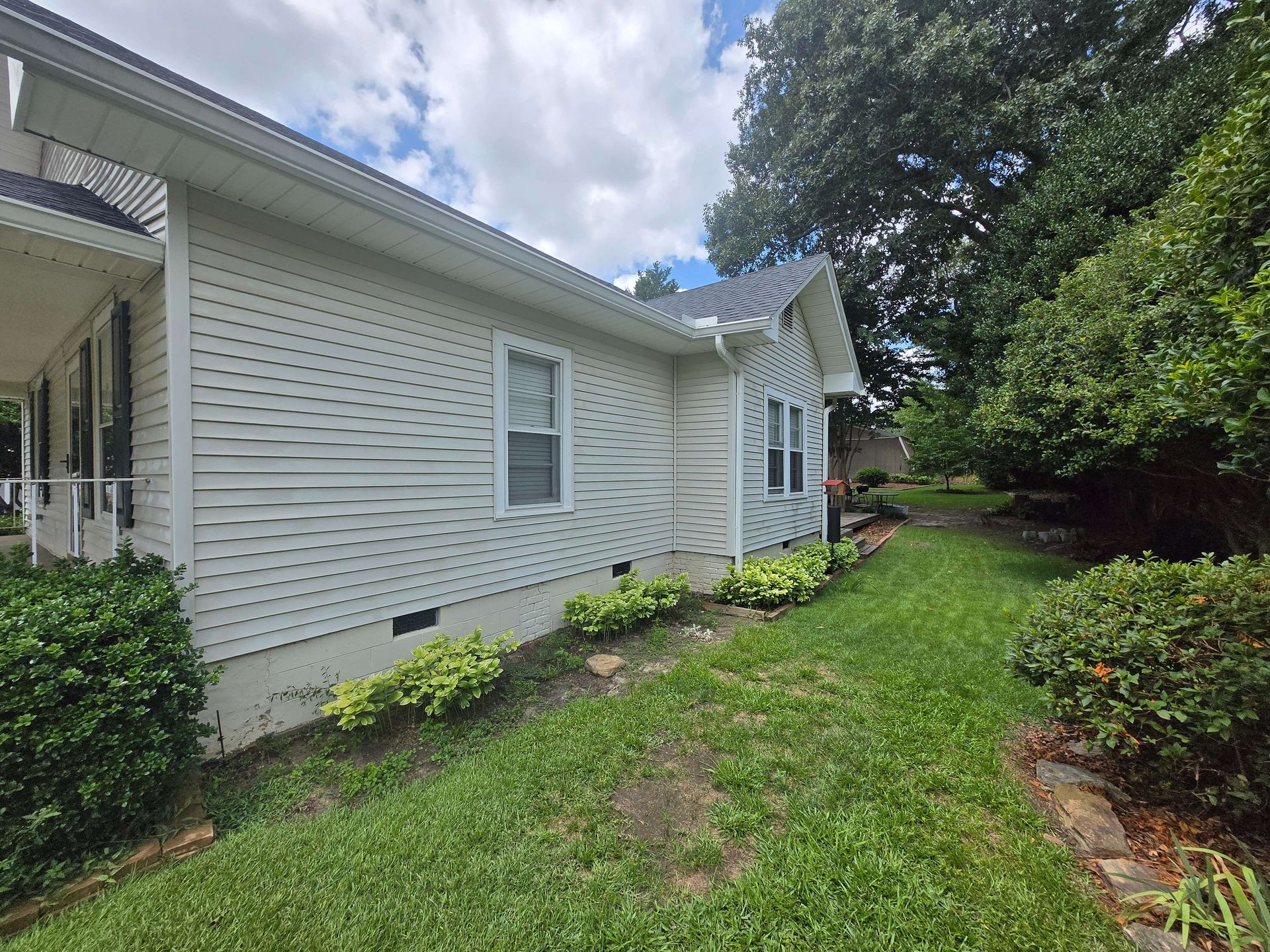White single-story house with vinyl siding and a grassy side yard under cloudy skies