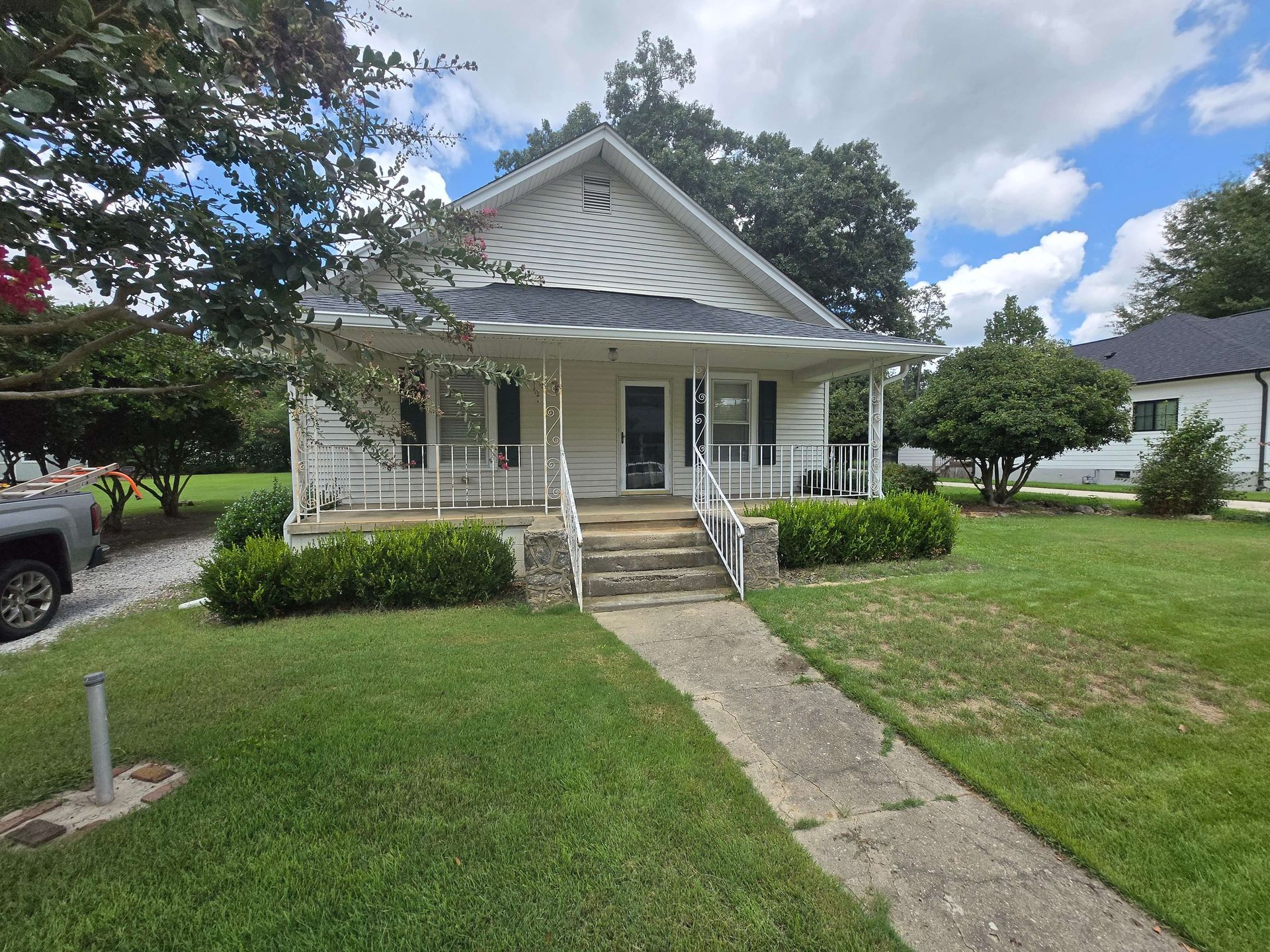 White bungalow house with front porch, steps, and a concrete walkway in a green suburban yard