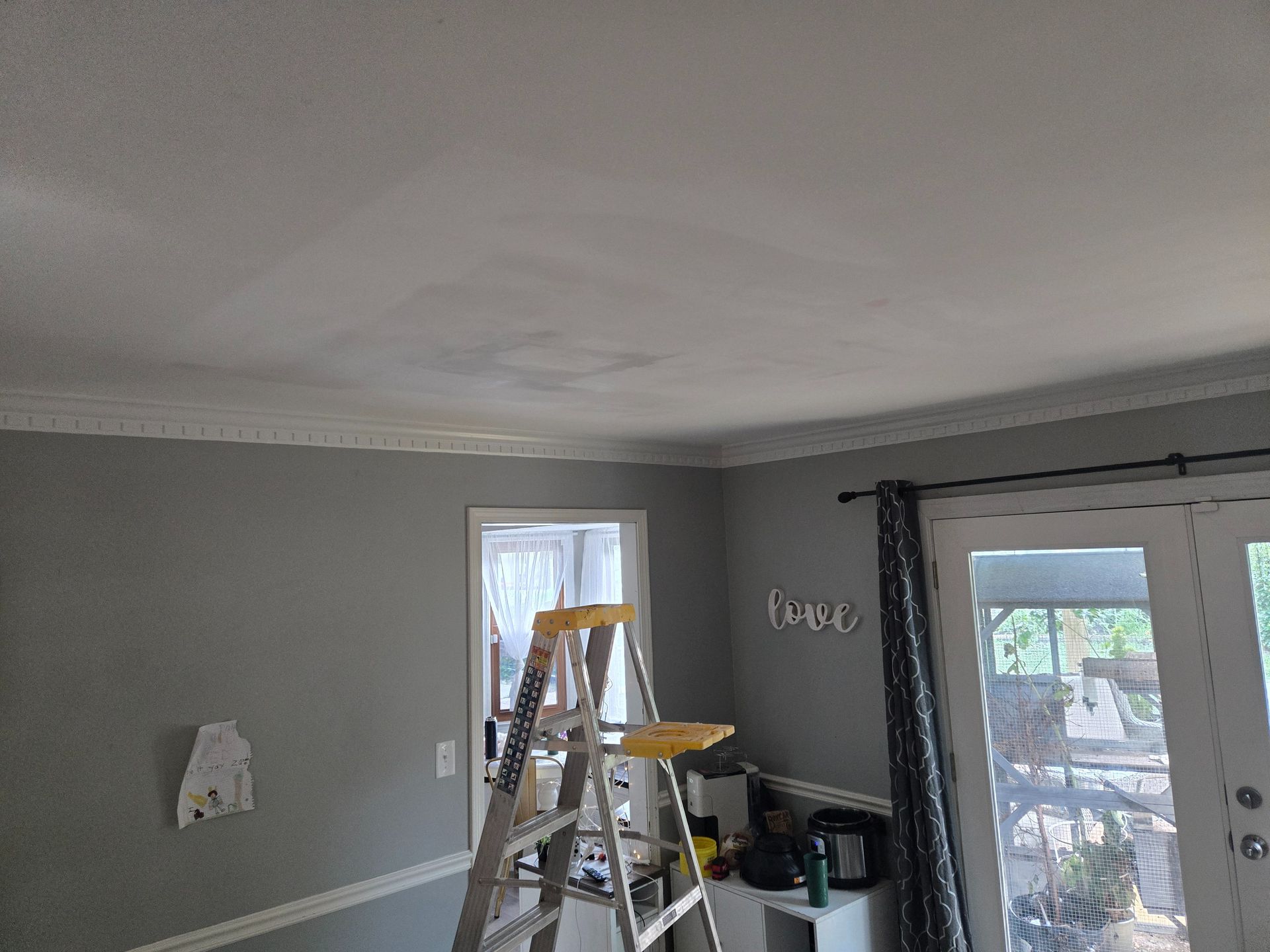 Gray room with ladder, chair, and tools near a window and double glass doors.