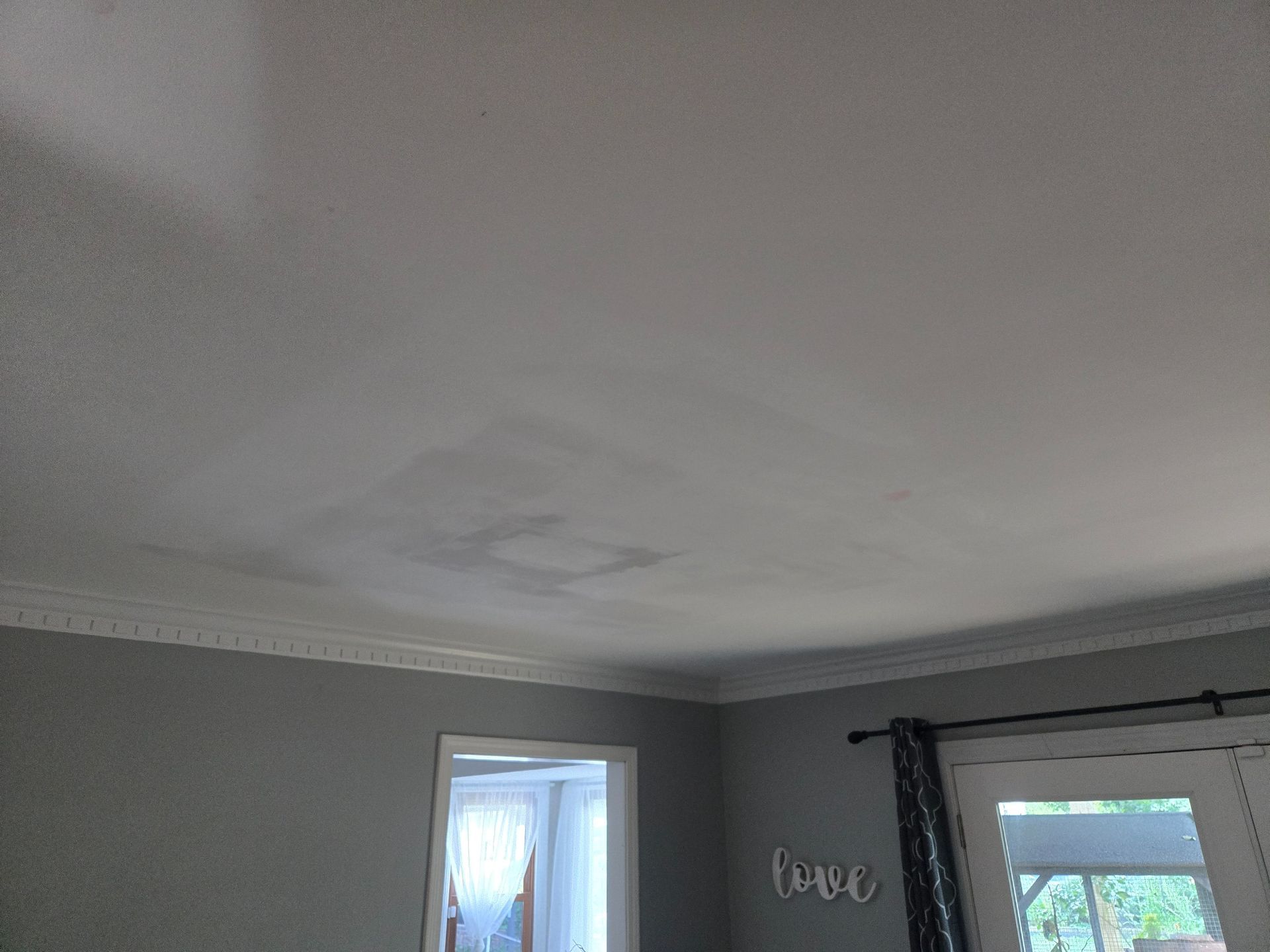 Gray bedroom corner with crown molding, a ceiling light spot, and a small window with dark curtains.