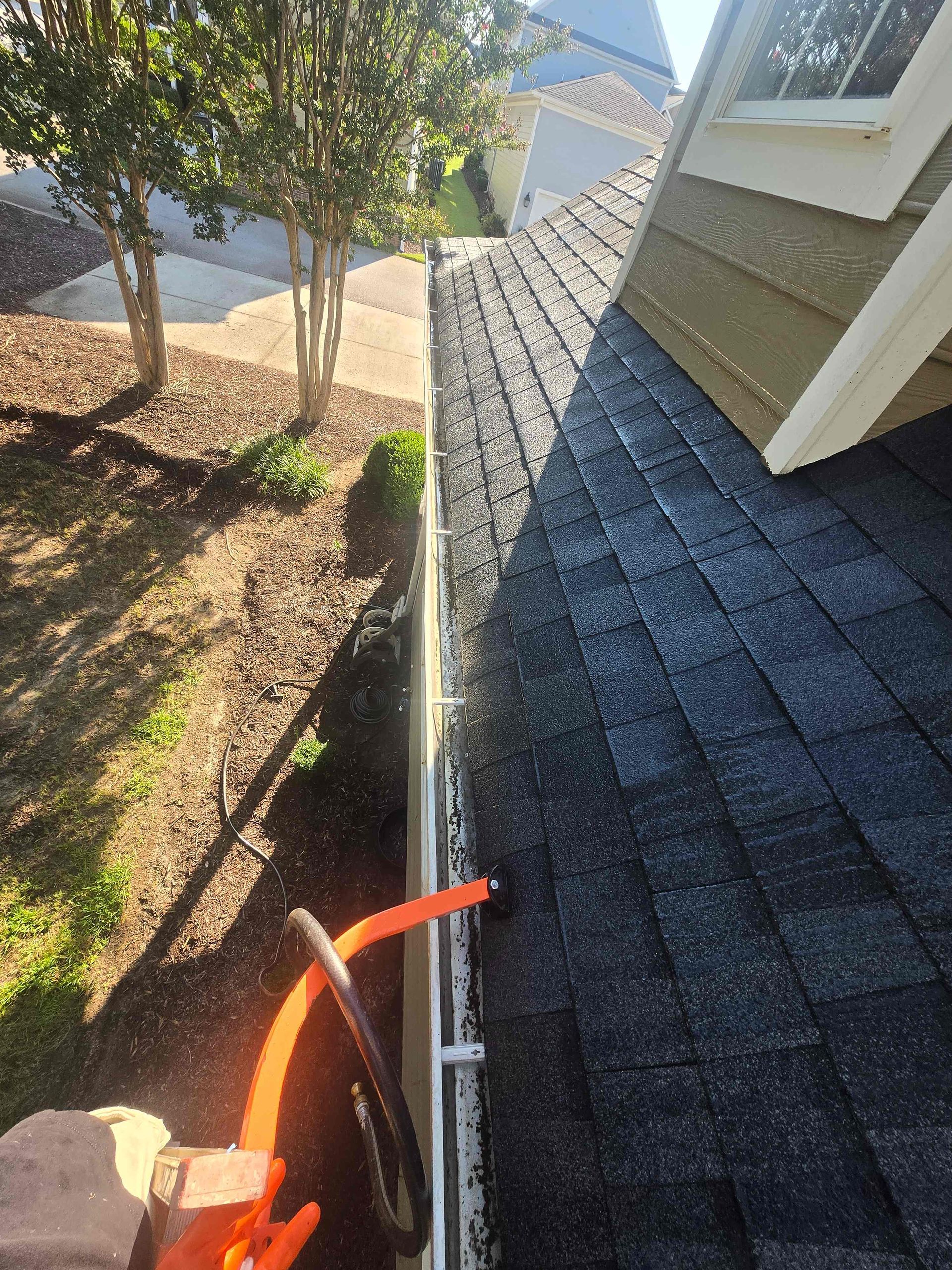 Roofing tools beside a house roof edge, with shingles and a yard below