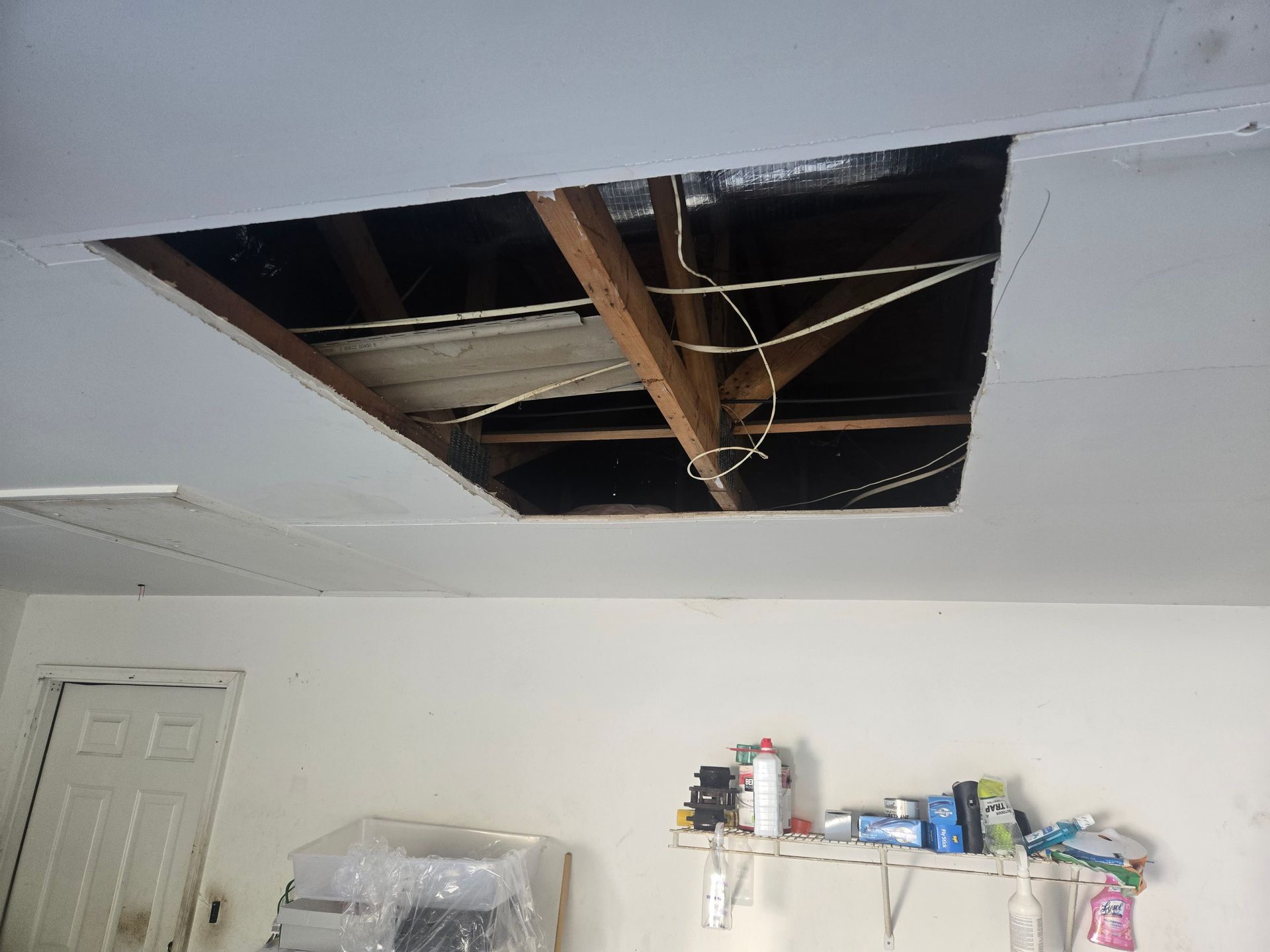 Damaged ceiling with a large open hole exposing wooden beams and wiring in a room under repair
