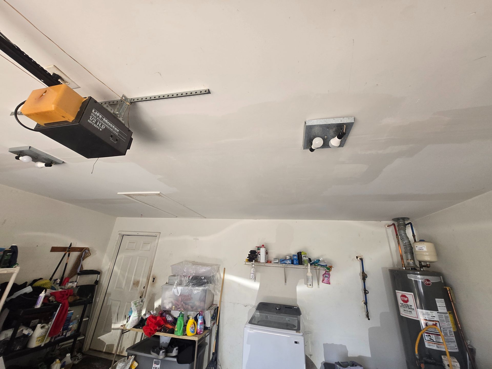 Garage interior with ceiling-mounted opener, shelves, tools, and a water heater