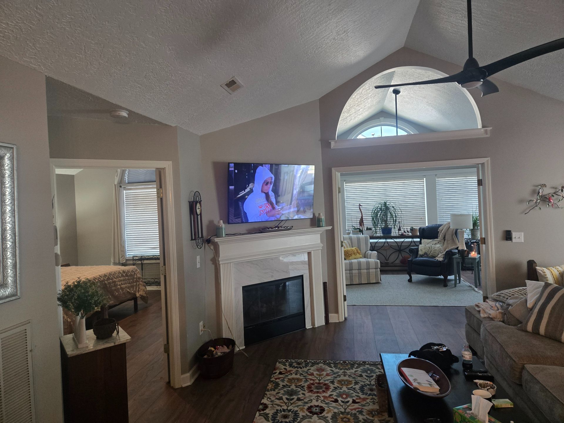 Living room with a TV above a fireplace, ceiling fan, and open doorway to a dining area.