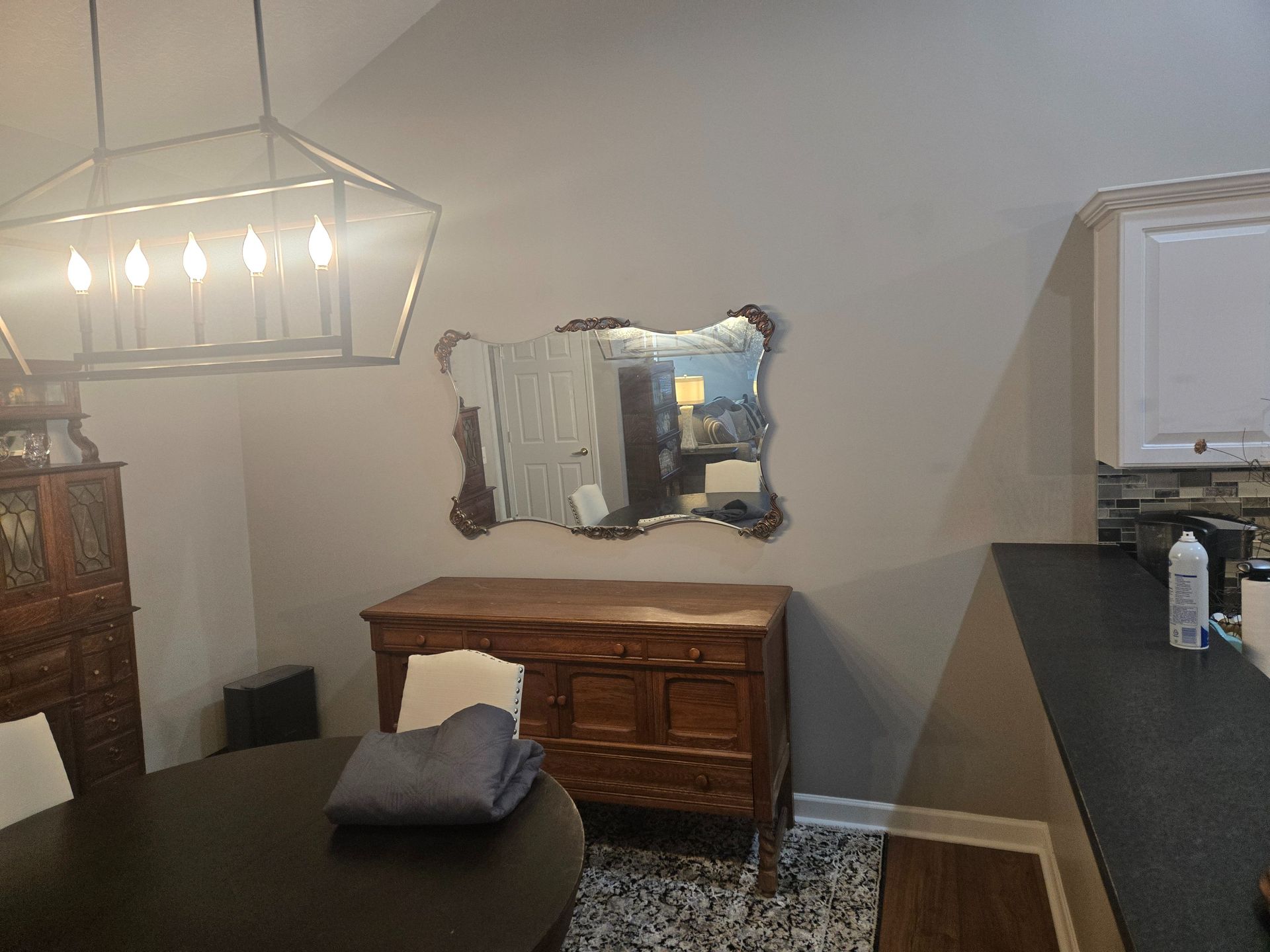 Dining room with chandelier, wooden sideboard, mirror, and black countertop beside a table with folded towels