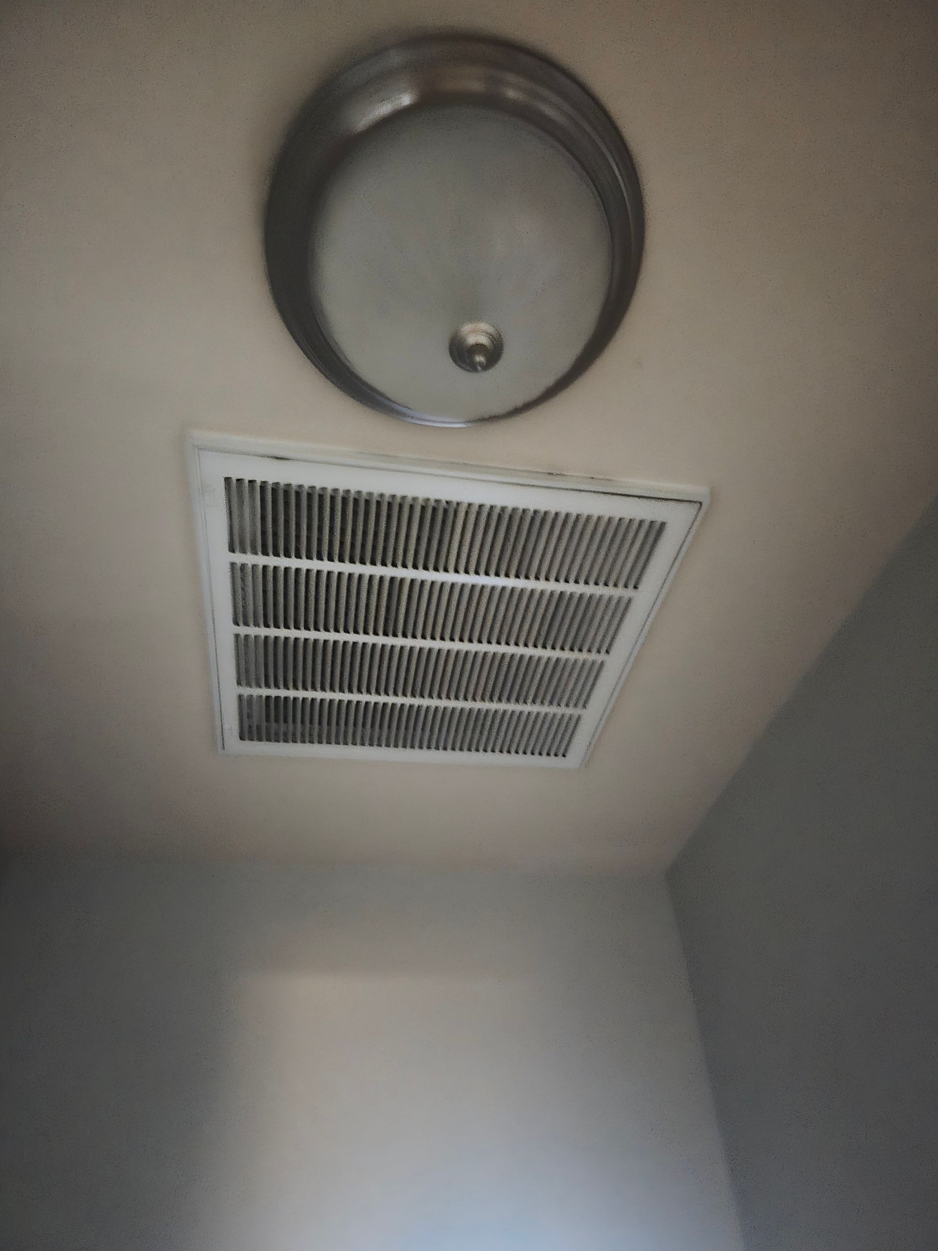 Ceiling vent and round light fixture in a plain white room.