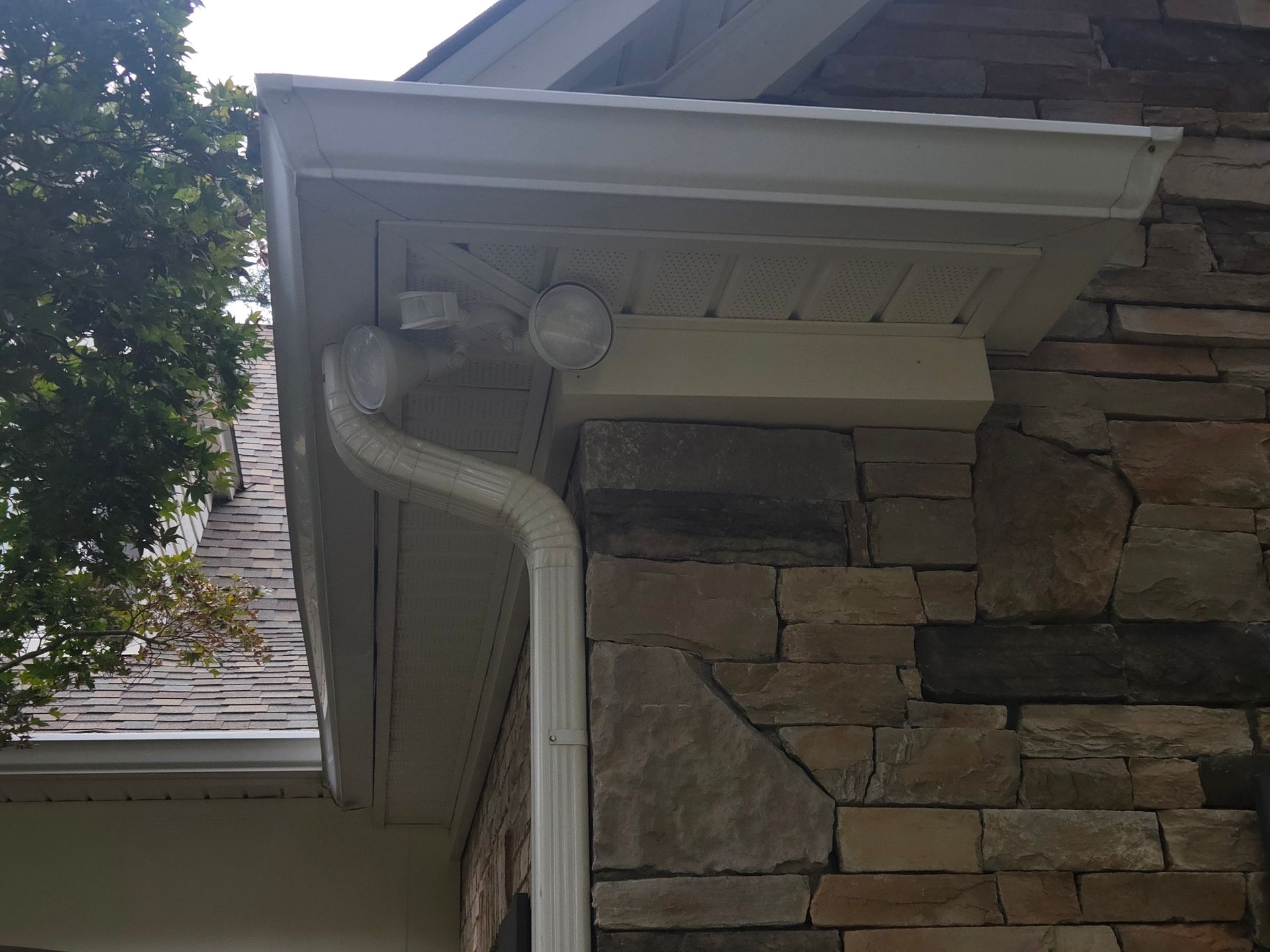White gutter and downspout on a stone house exterior under a roof overhang