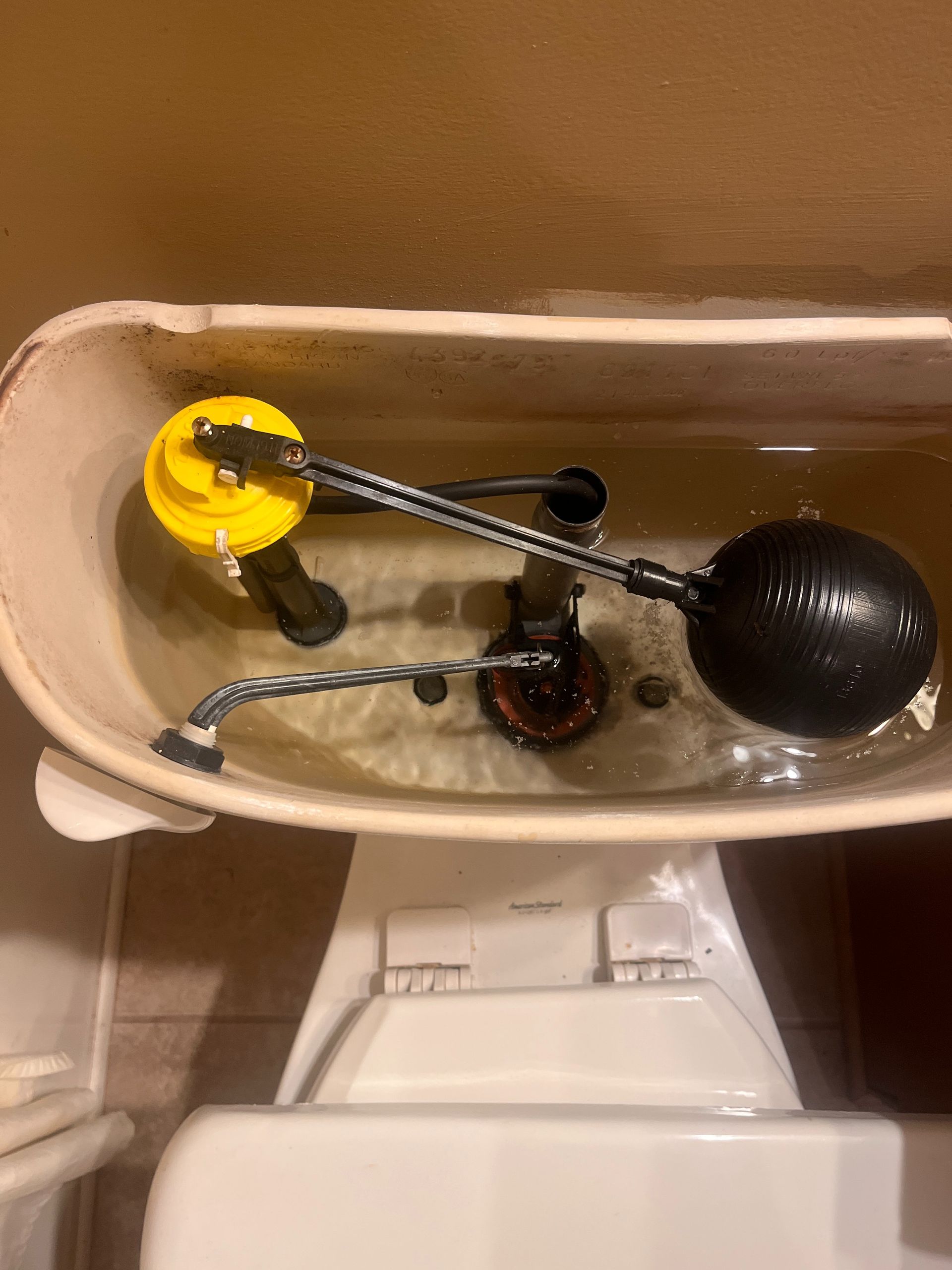 Toilet tank with a yellow-and-black float valve assembly inside.