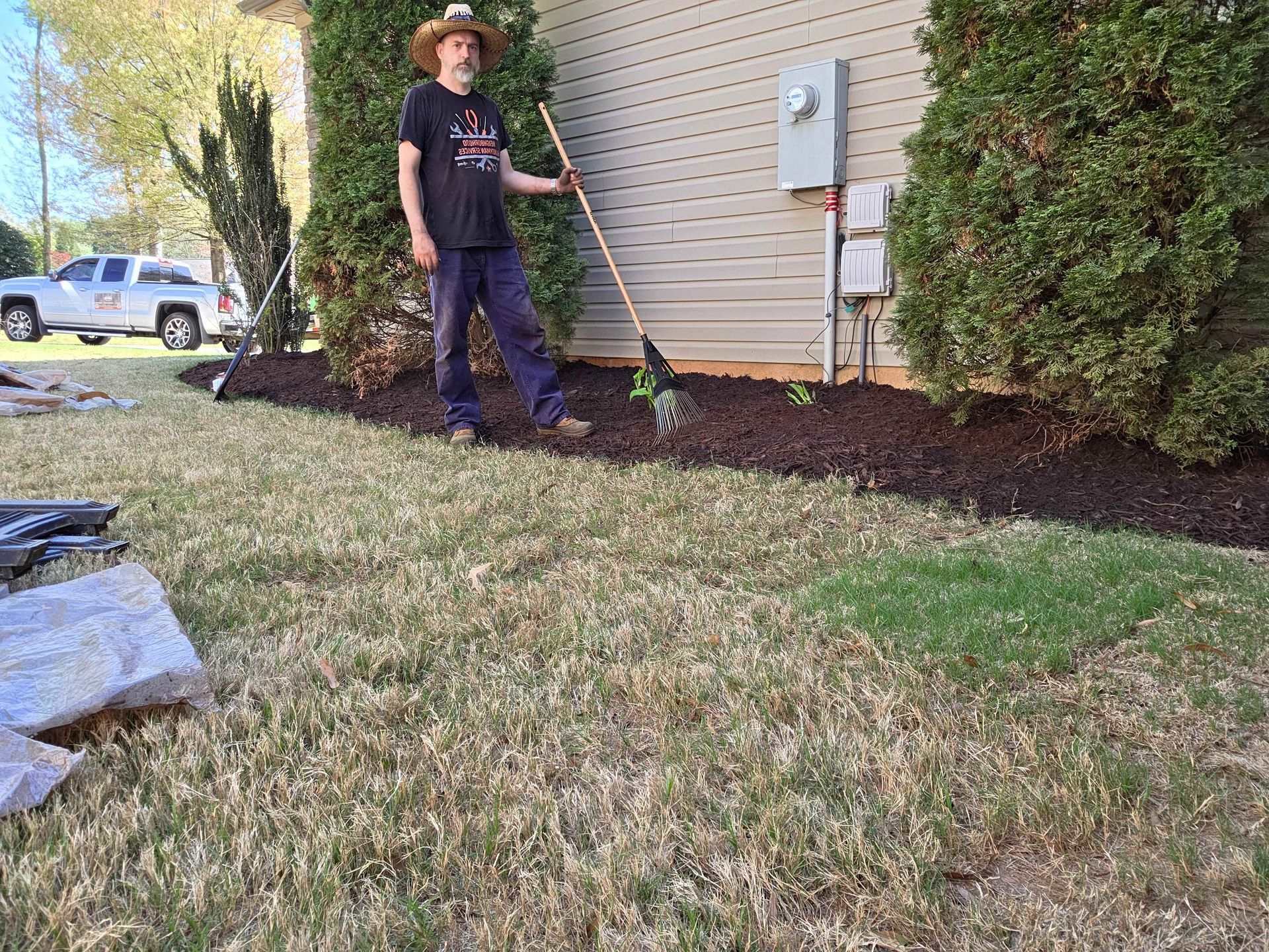 Person edging mulch along a house wall with a string trimmer in a yard