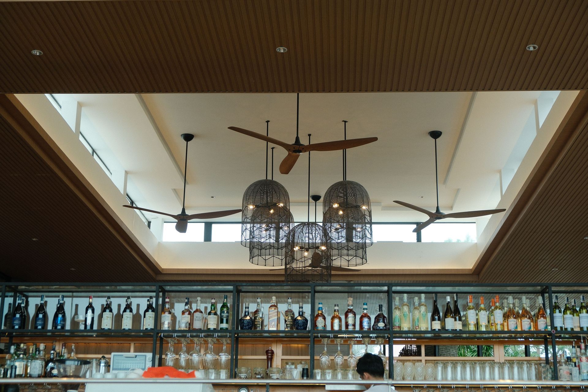 Modern bar interior with large windows, hanging lanterns, and rows of bottles on shelves