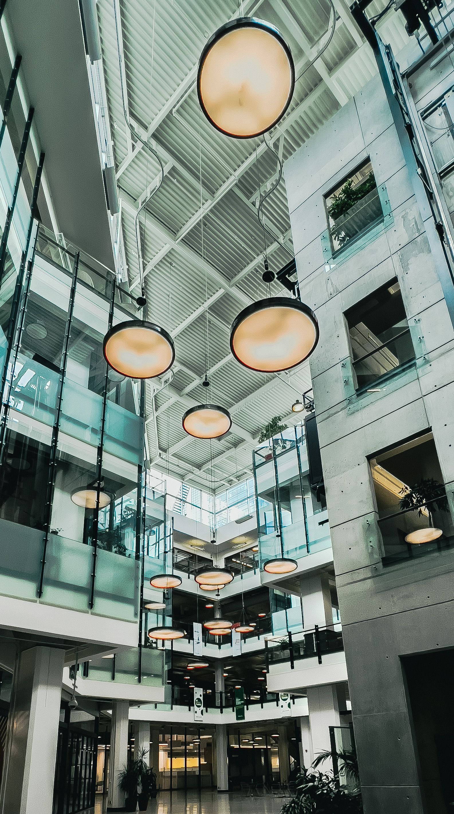 Modern atrium with glass walls, hanging round lights, and multiple balconies looking upward