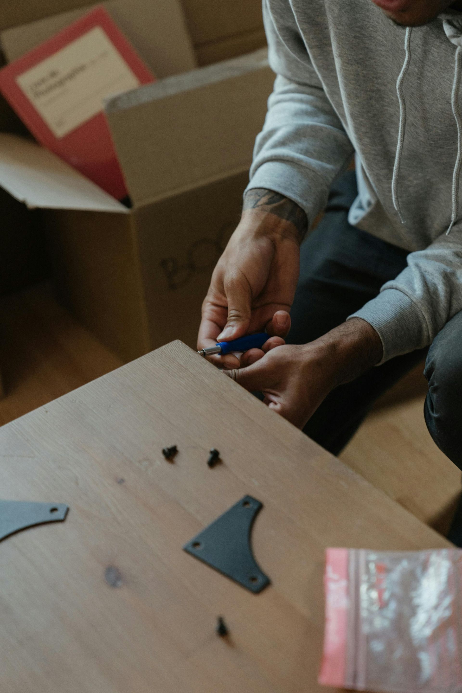 Person assembling furniture, screwing metal bracket to a wooden surface.