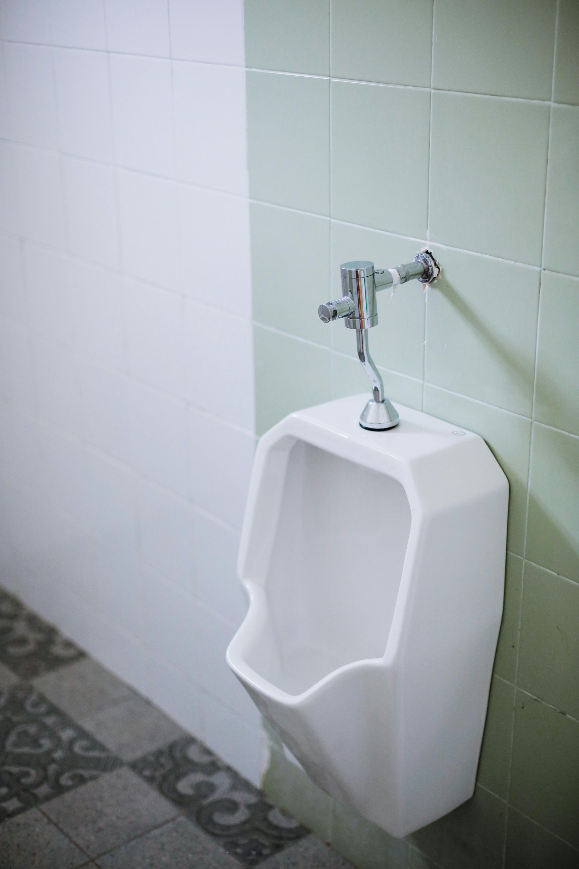White urinal on a tiled wall; gray and green tile floor.