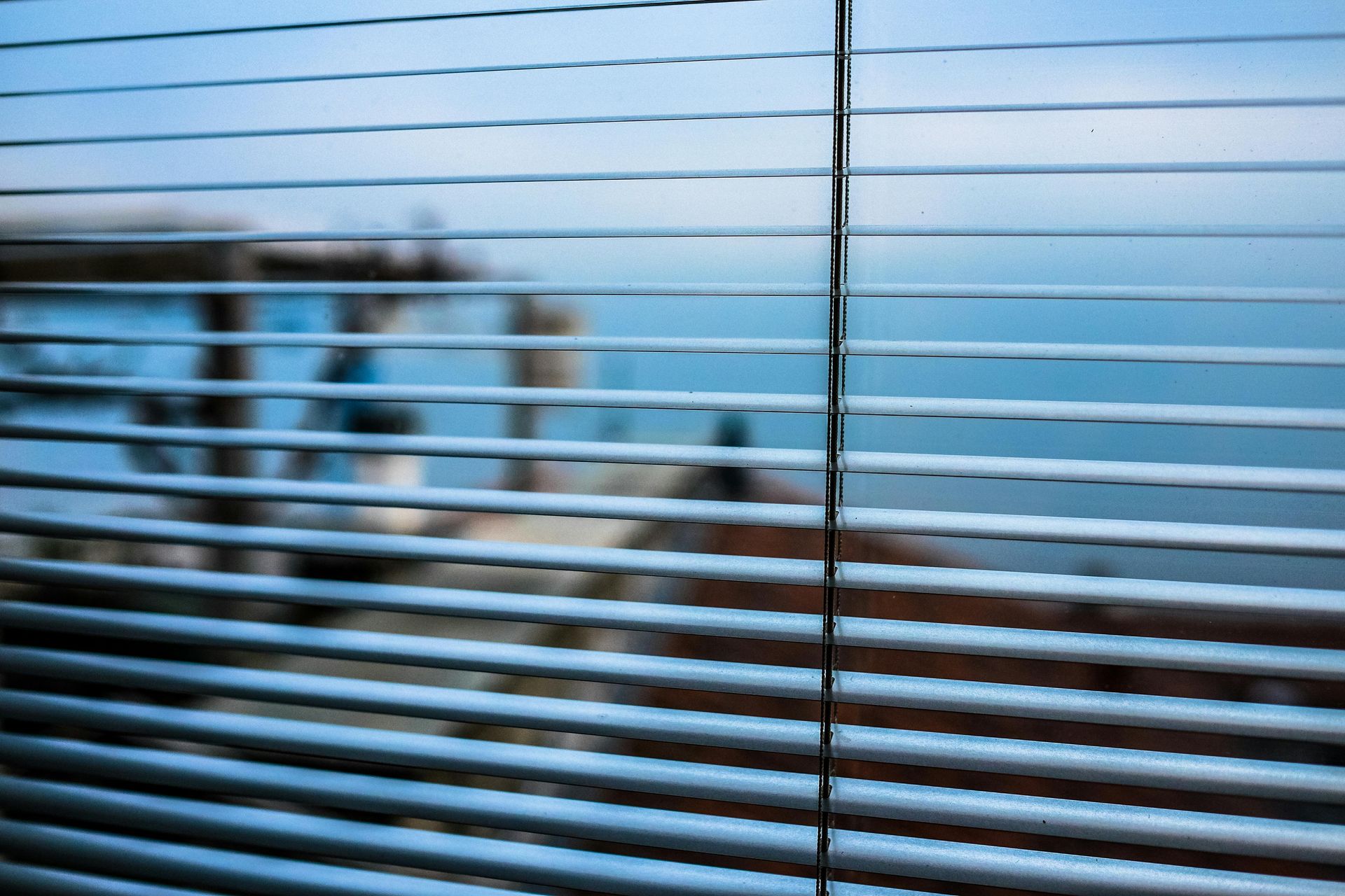 View through horizontal blinds: blurred waterfront scene; blue sky, water, dock.