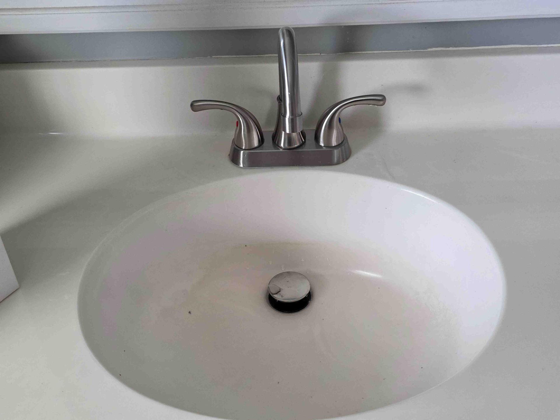 A white bathroom sink with a silver, two-handle faucet and a black drain plug in a white countertop.