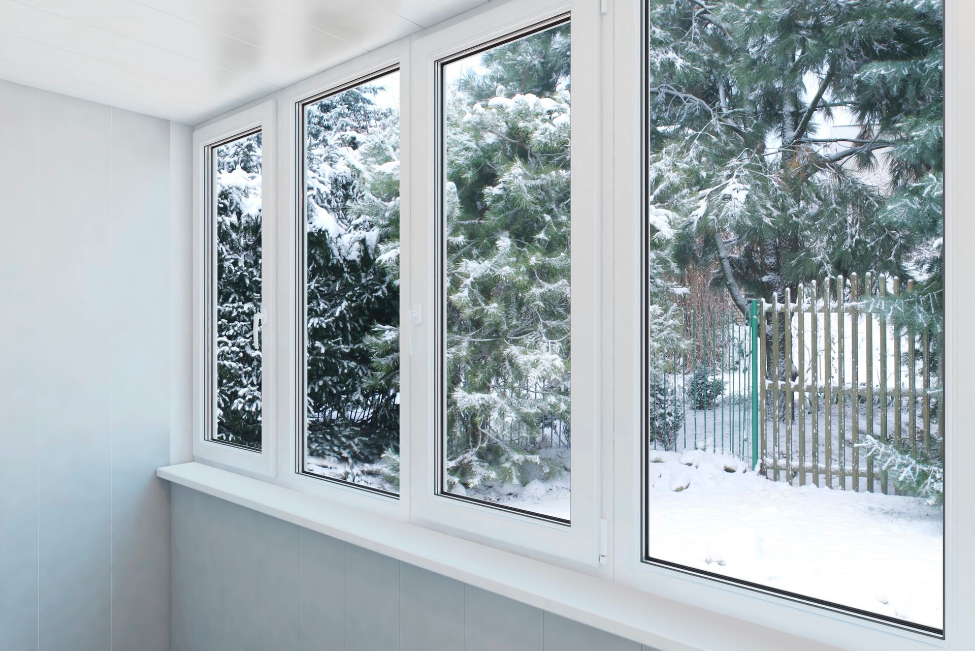 White-framed windows looking out at snow-covered trees and a fence. Inside, a white sill and wall.