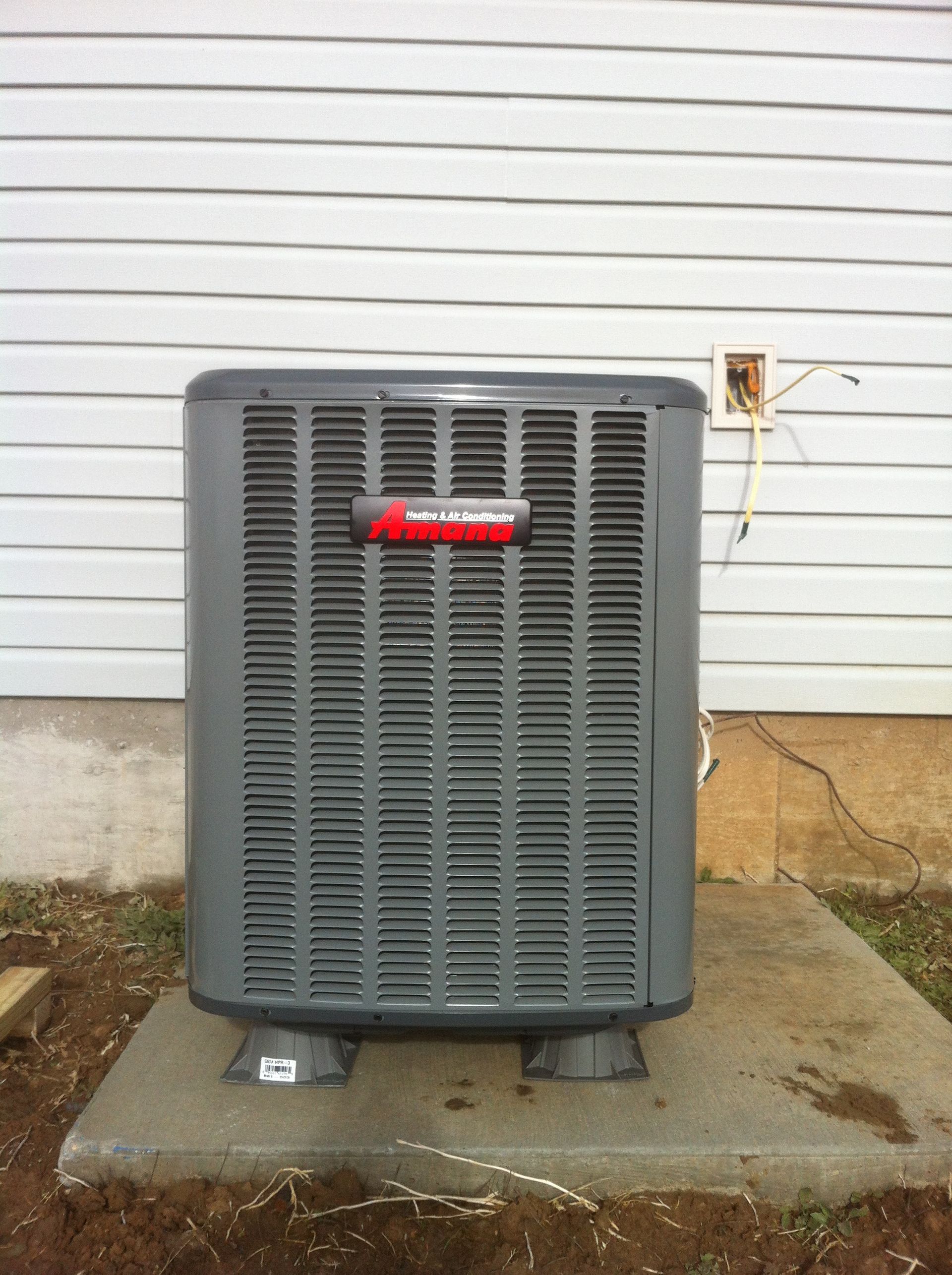 A gray air conditioner is sitting outside of a house
