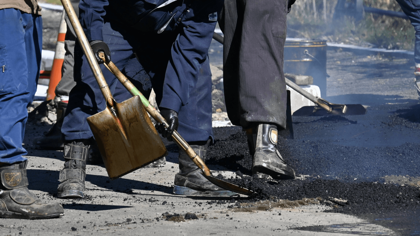 Workers using shovels to spread and level hot asphalt on a damaged road section during an asphalt paving service in Highlands Ranch, CO