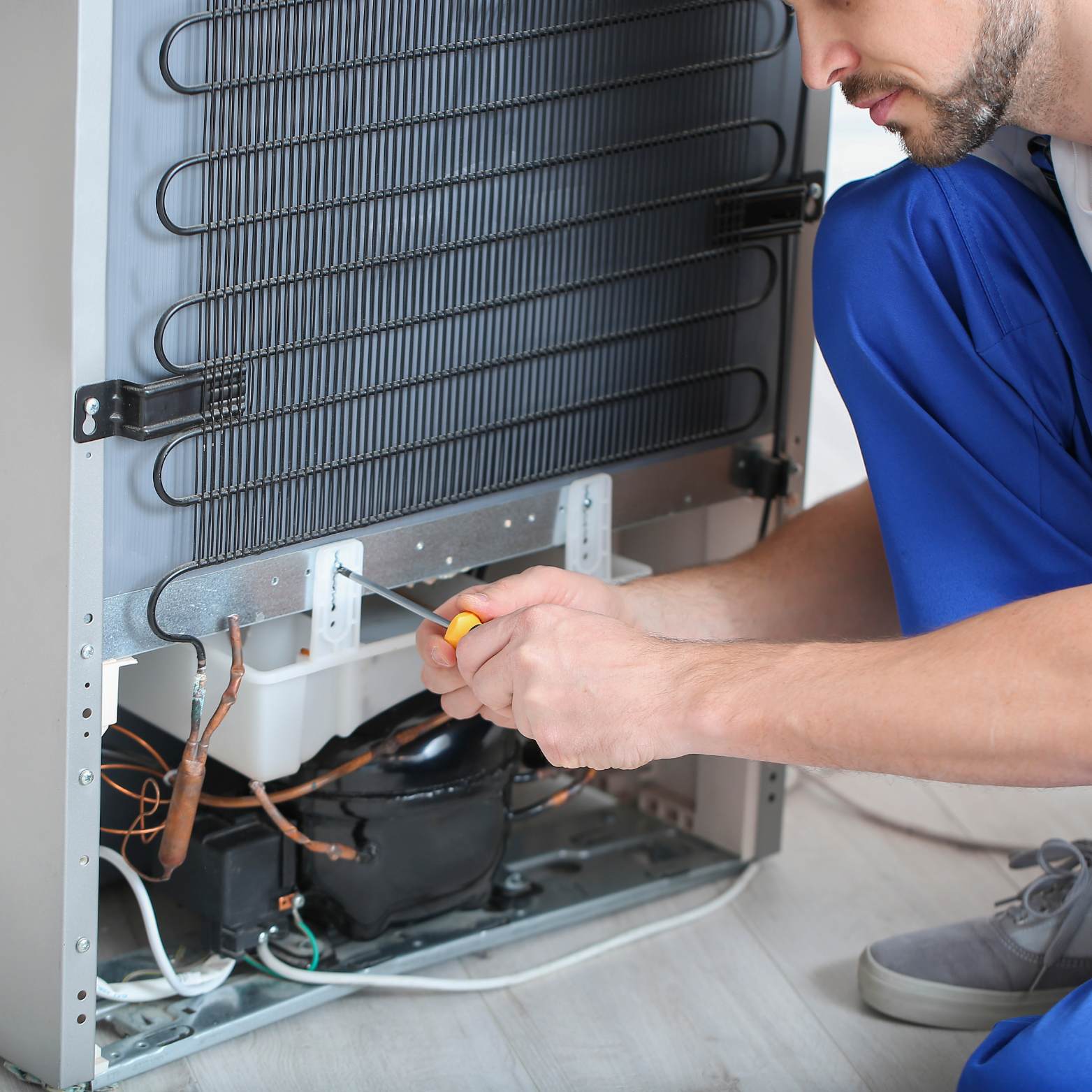 A man is working on a refrigerator with a screwdriver