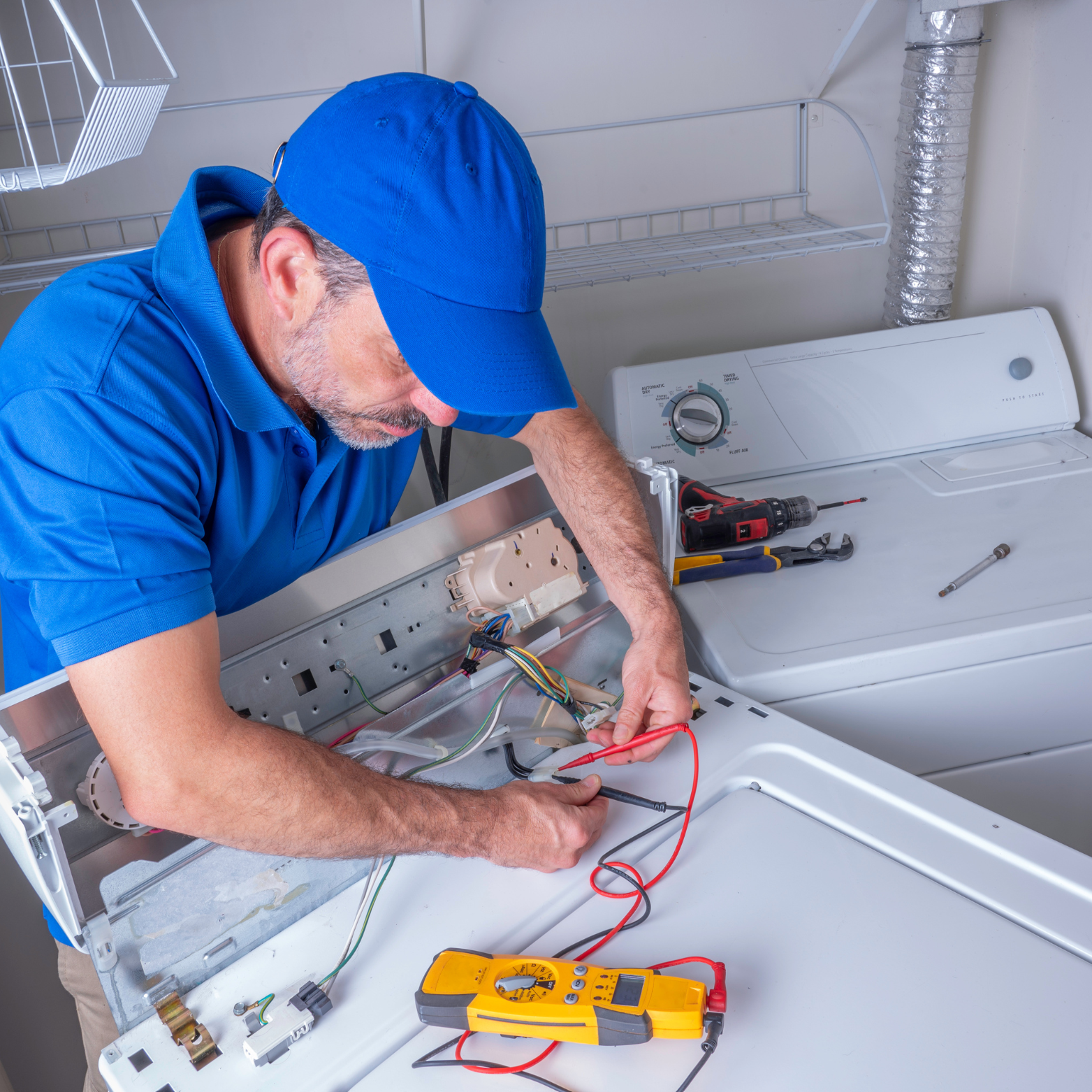 A man in a blue hat is working on a washing machine