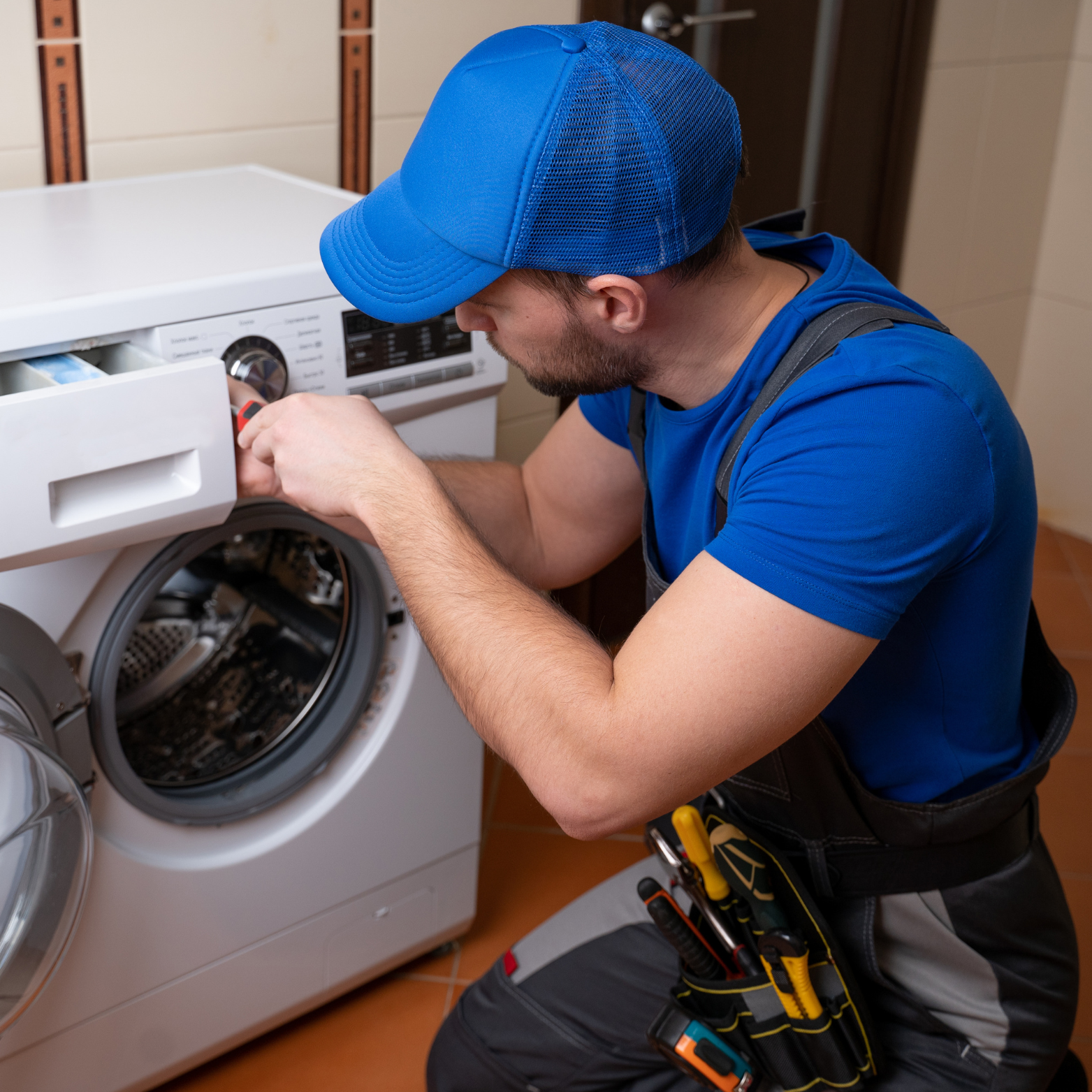 A man wearing a blue hat is working on a washing machine