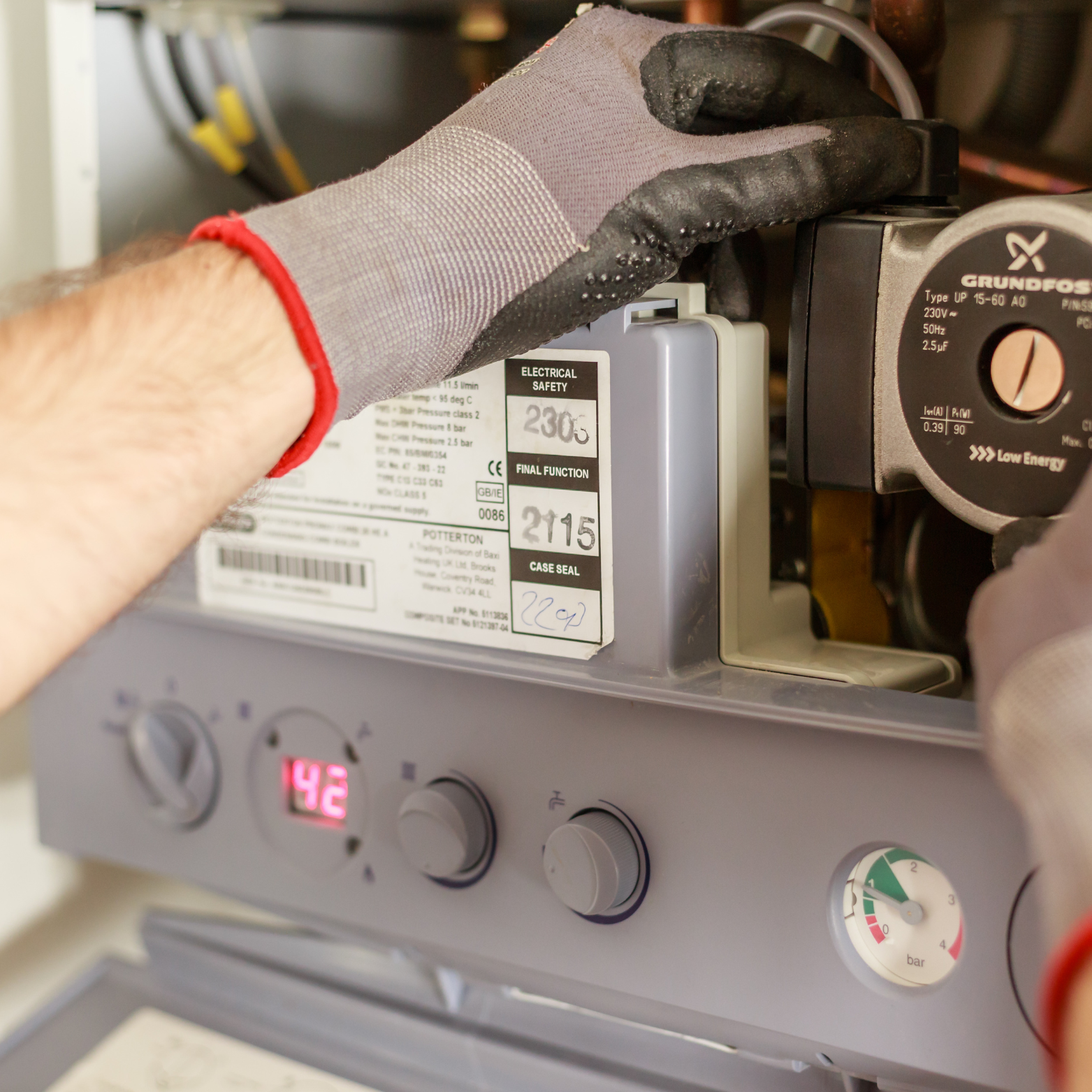A person wearing gloves is working on a boiler that has the number 212 on it