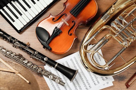 A violin , clarinet , trumpet , and piano keyboard are on a wooden table.
