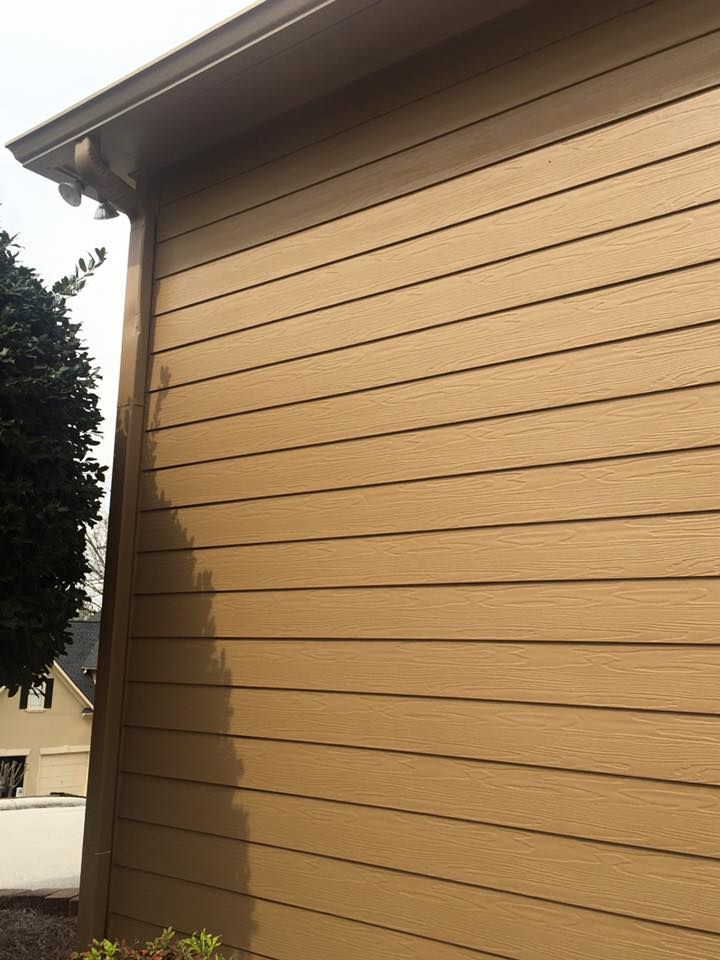 Tan horizontal siding on the exterior of a house, seen from the corner near a roof overhang and a green tree.