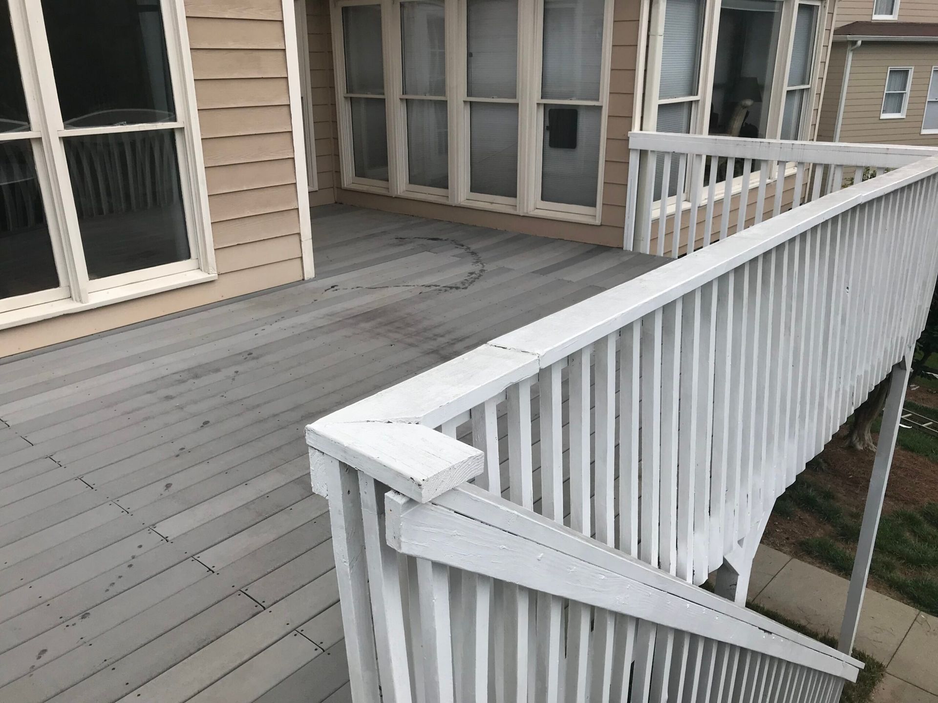 An elevated wooden deck with grey planks and a white railing overlooking a building exterior.