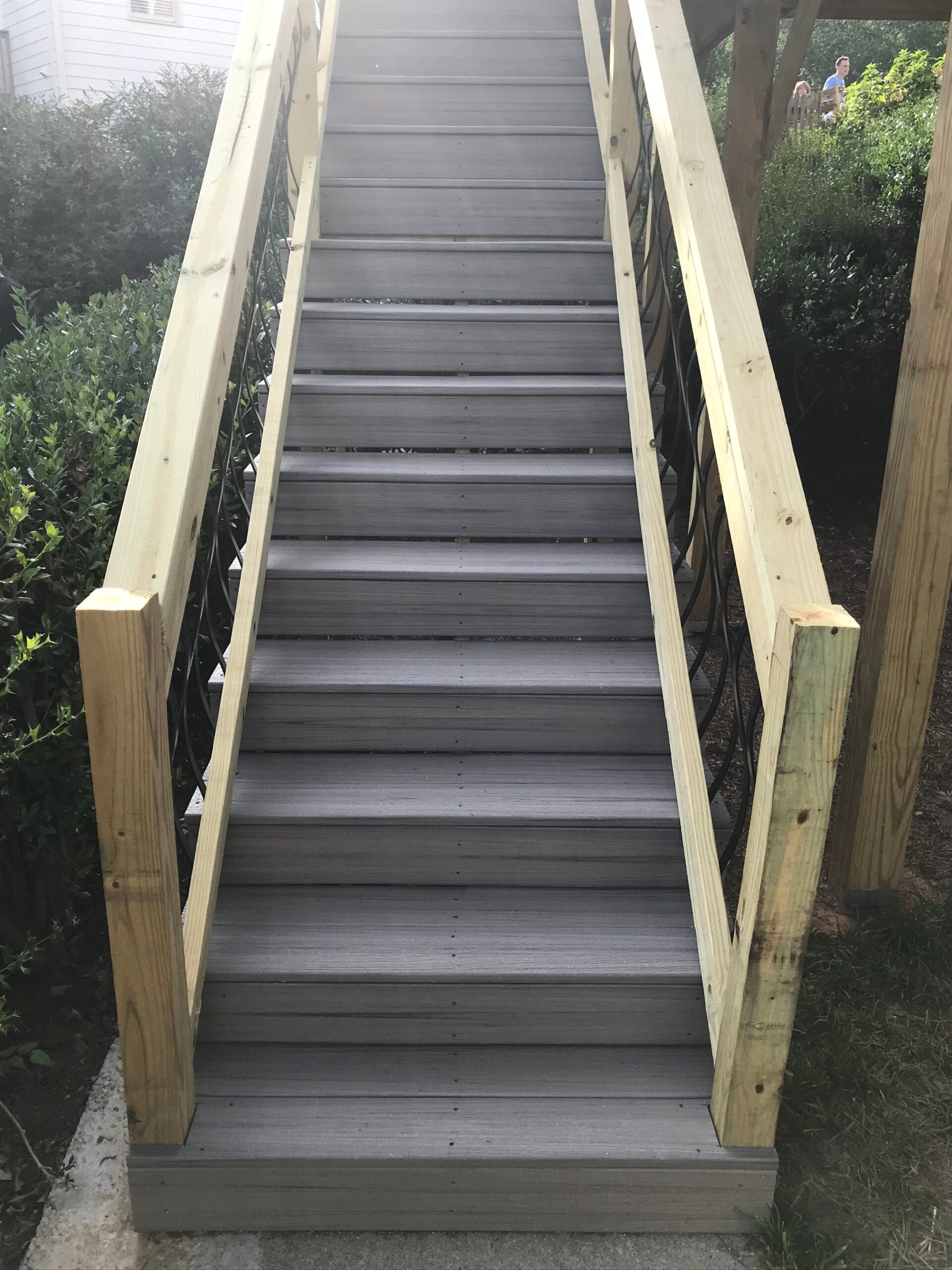 Straight staircase with gray wooden treads and light-colored wooden handrails outdoors.