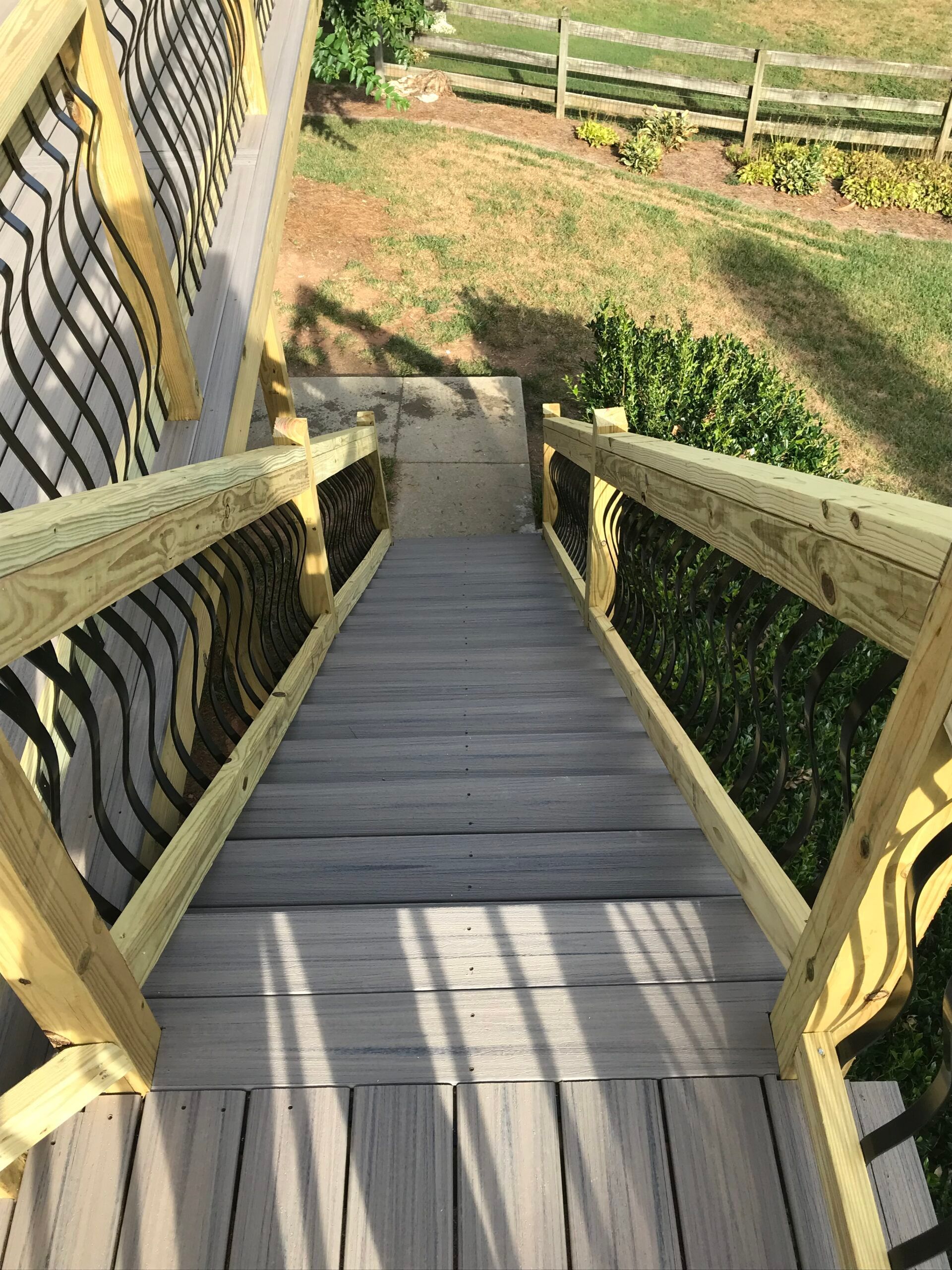 A downward view of outdoor wooden stairs with railings, leading to a landing on a grassy yard.