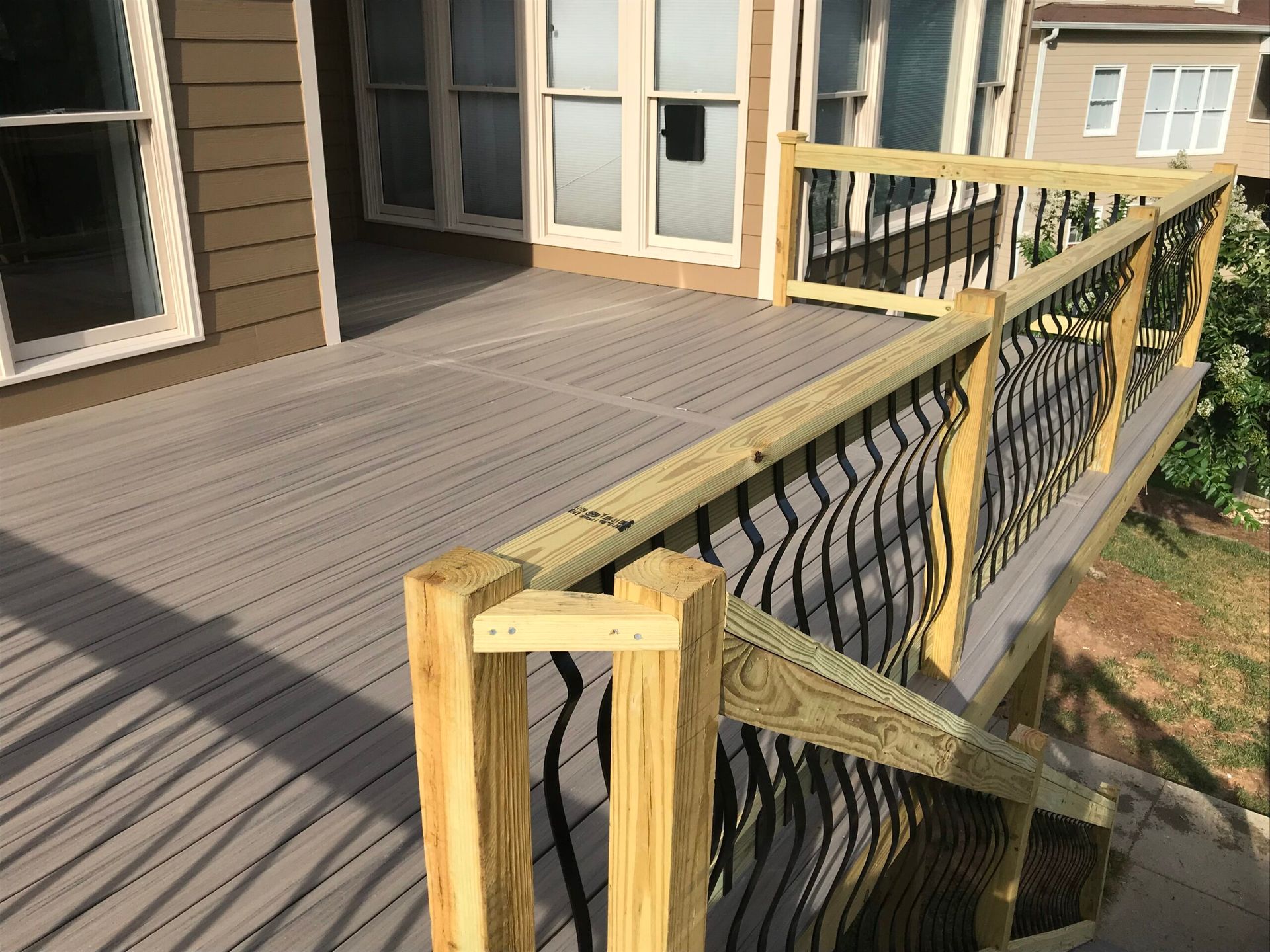 A wooden deck featuring gray composite boards and railings with black metal balusters, extending from a house.