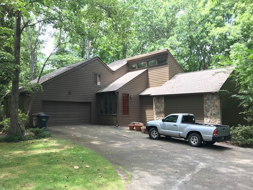 A brown, multi-level house with a stone accent, a two-car garage, and a silver pickup truck parked in the driveway.