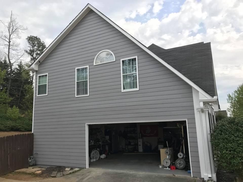 A gray, two-story house with a wide-open garage, a triangular roofline, and three windows on the side exterior.