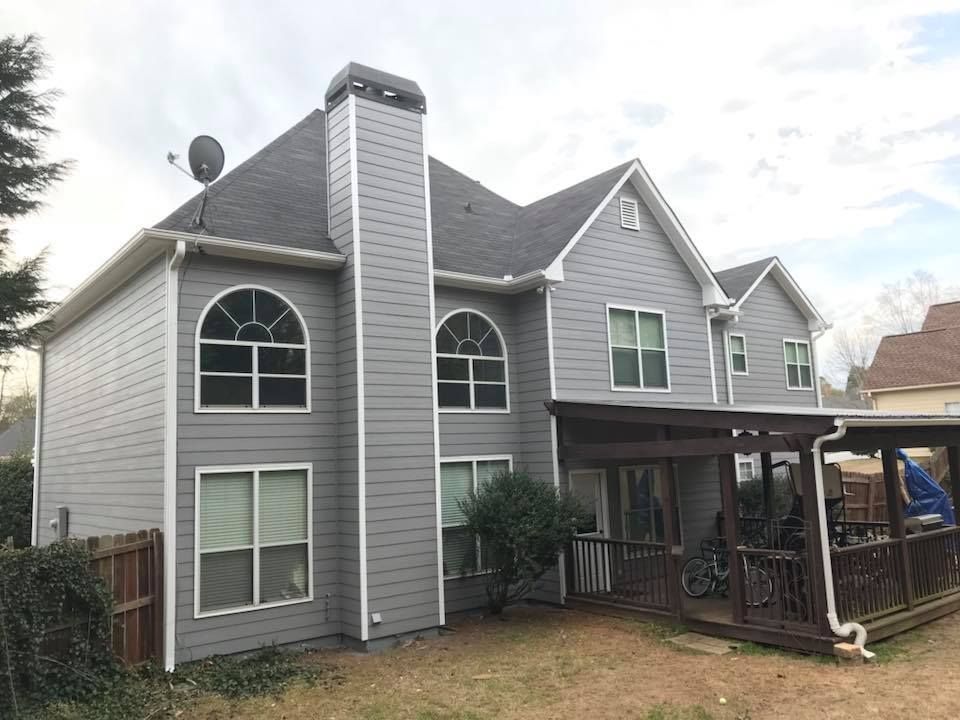 Two-story house with gray horizontal siding, a large chimney, arched windows, and a covered back deck.