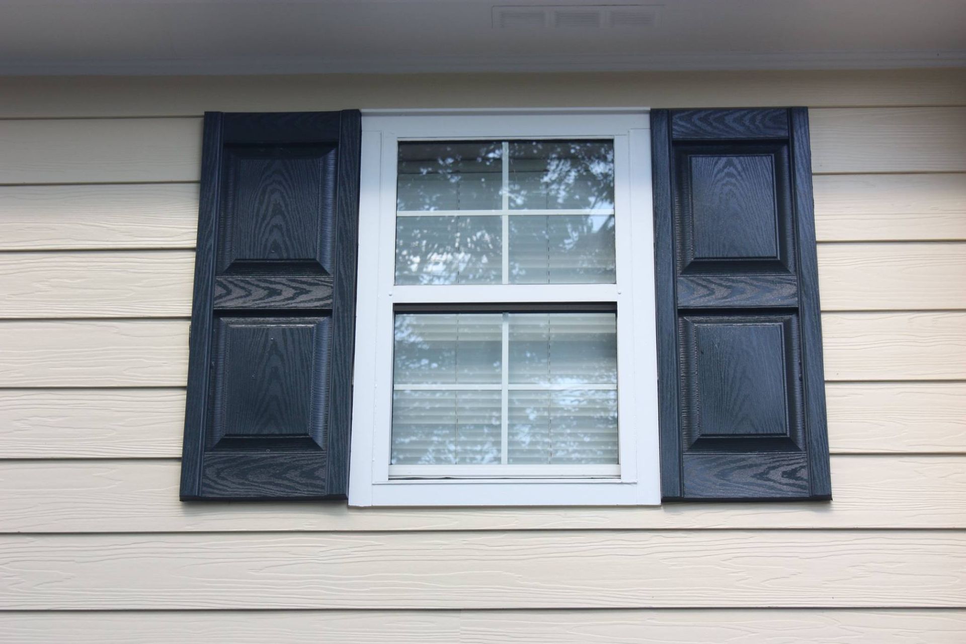A white-framed window with black shutters, mounted on light tan horizontal siding.