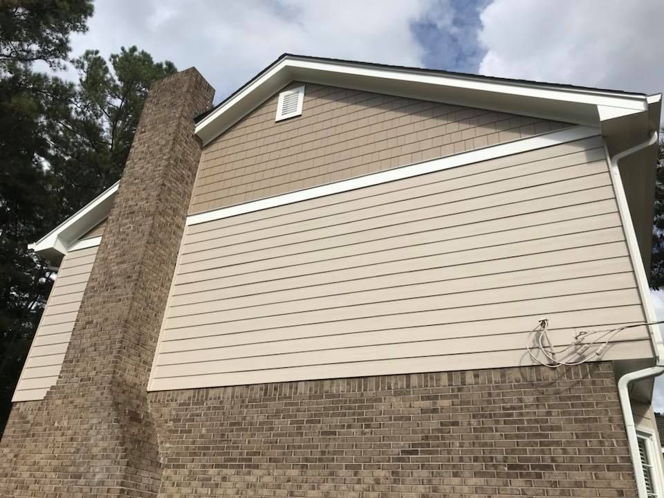 A side view of a house exterior featuring a brick chimney, tan horizontal siding, and light brown shake shingles.