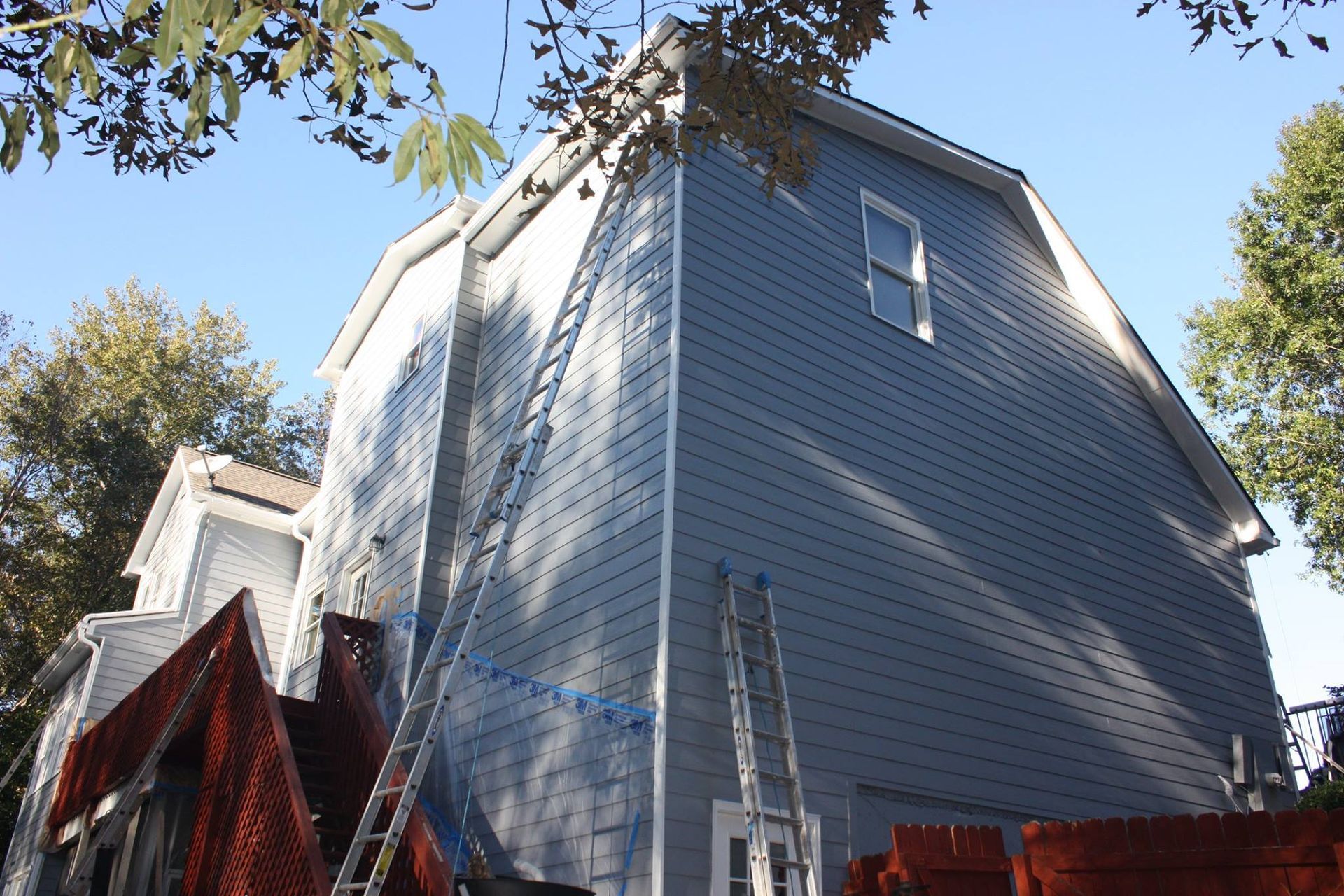 Blue siding on a multi-story house under construction, with two ladders leaning against the exterior walls.