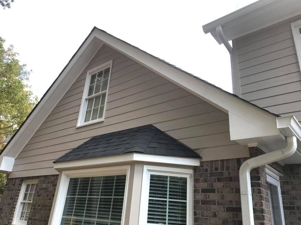 Exterior view of a house with brown horizontal siding, a brick base, black roof shingles, and white-framed windows.