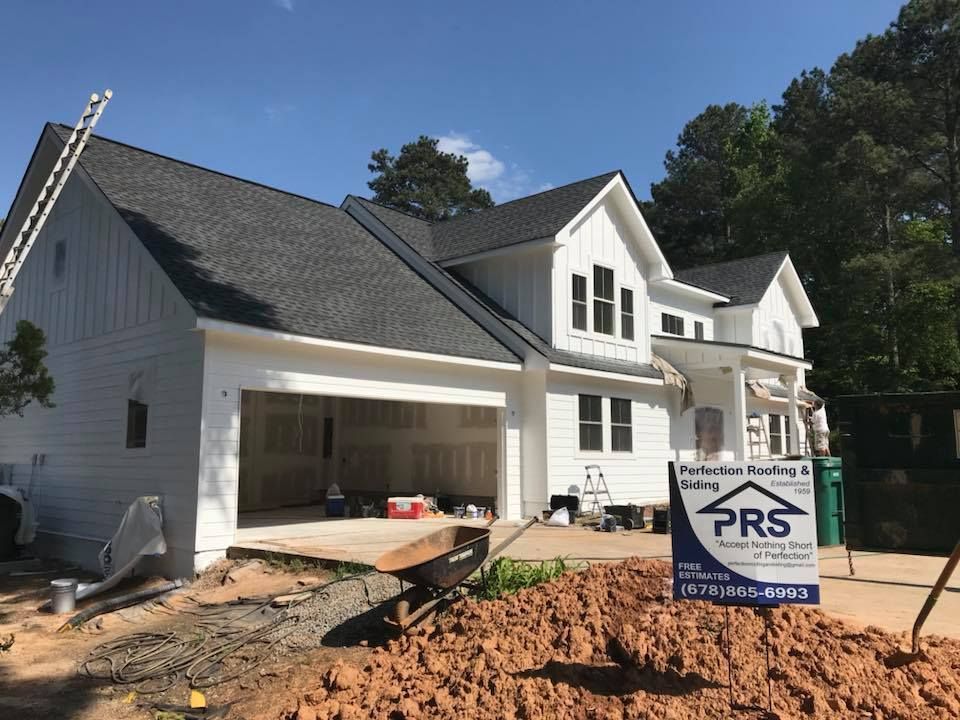 Newly built white house with a gray shingled roof, a garage, and a construction sign in the foreground.