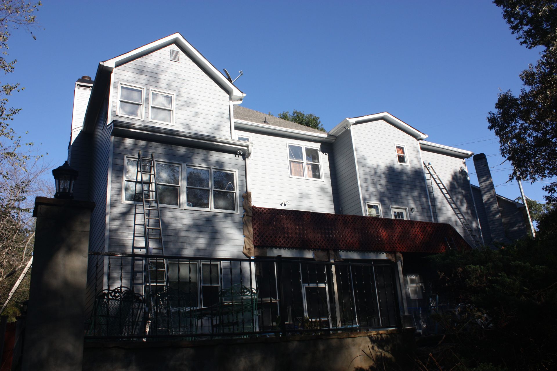 A light gray two-story house with a red awning and a dark metal balcony on a sunny day.