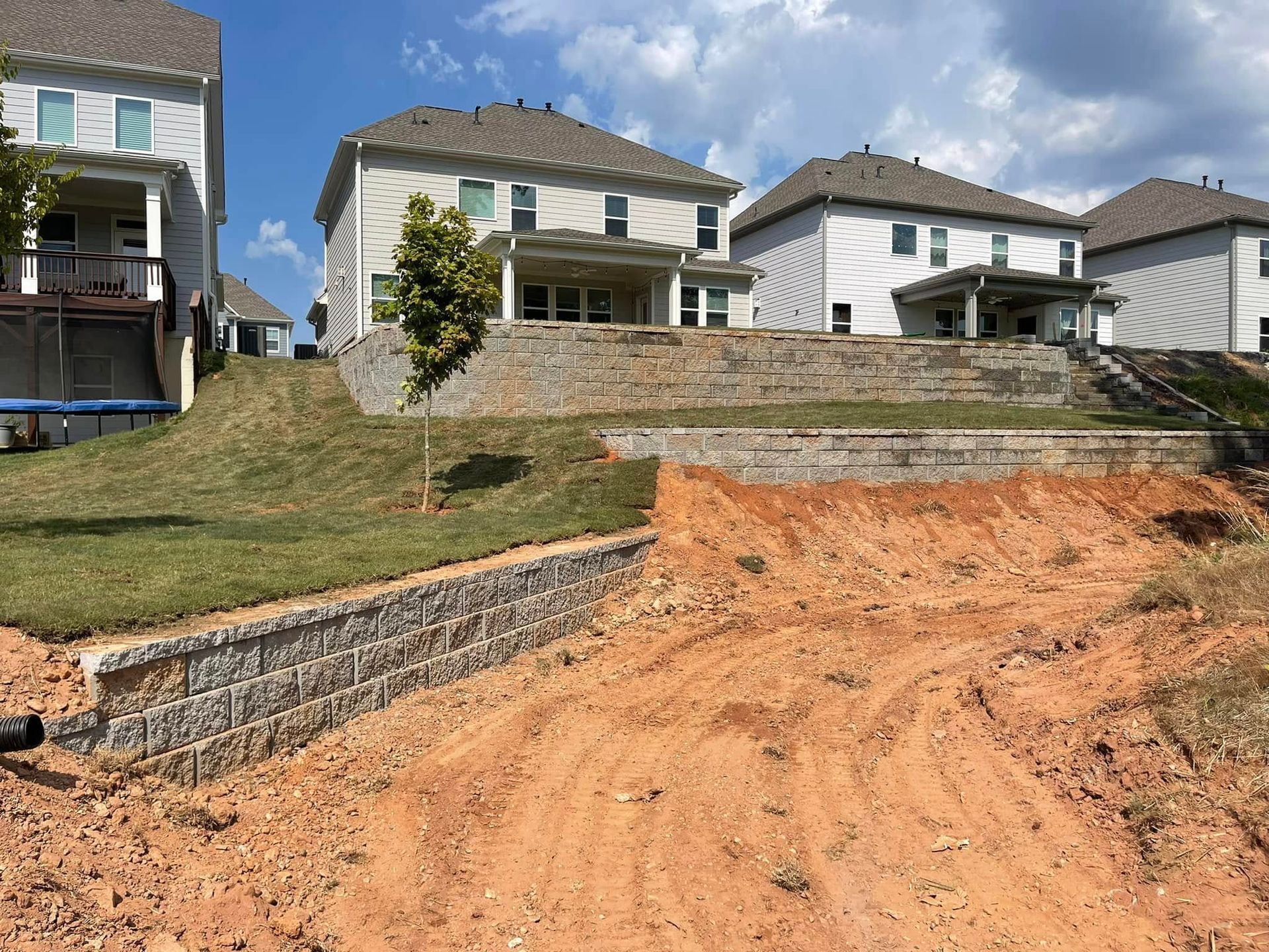 New homes on a hillside with unfinished dirt driveway and retaining walls