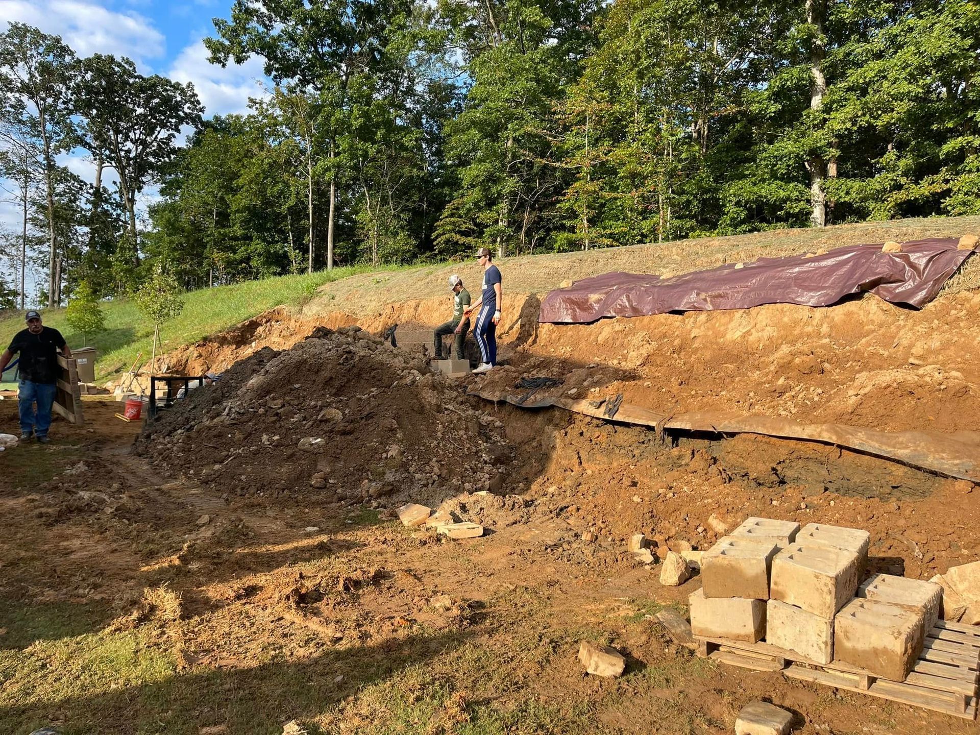 Construction site on a hillside with workers, exposed soil, and stacked blocks in the foreground