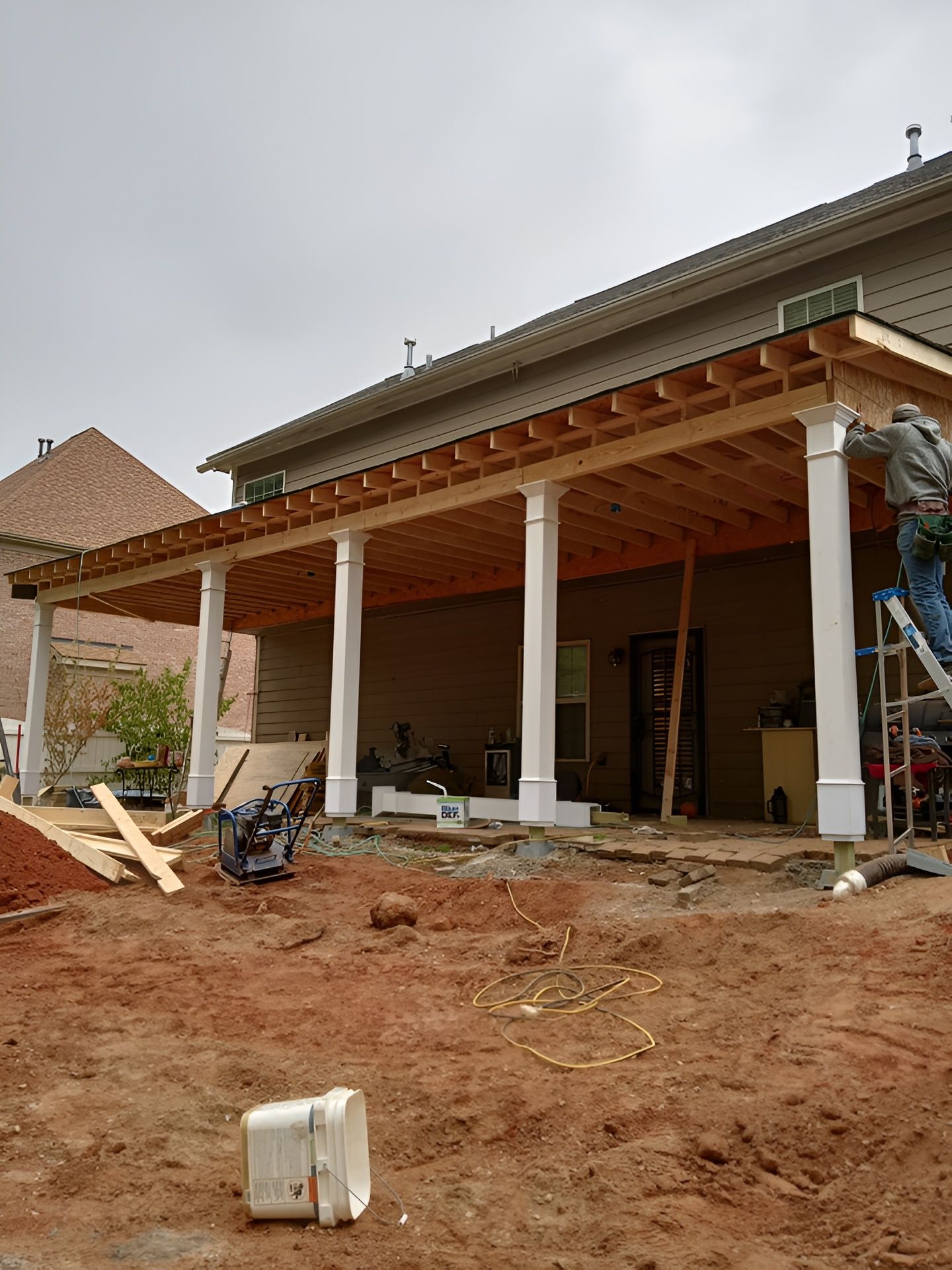 Partially built house with a covered porch, construction materials, and dirt foreground